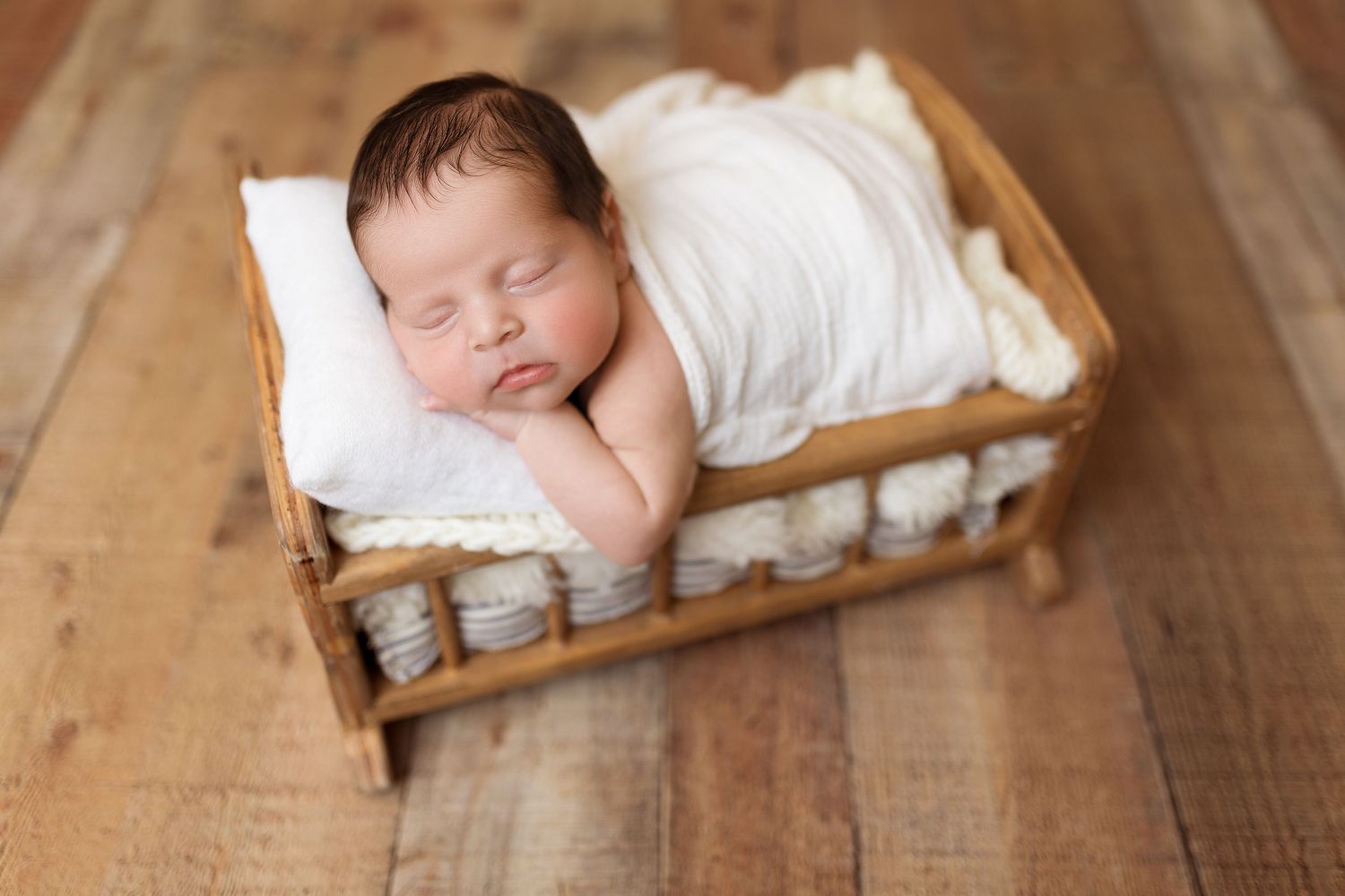 Peaceful newborn sleeps on white cushion in rustic wooden crate.