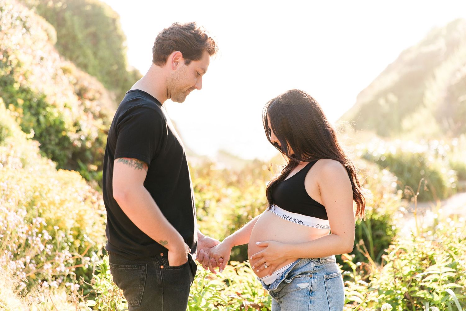 Couple shares intimate moment during sunset maternity photoshoot in natural setting.