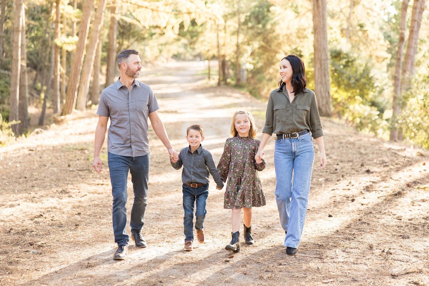 Family walking together through a sunlit forest path during golden hour.