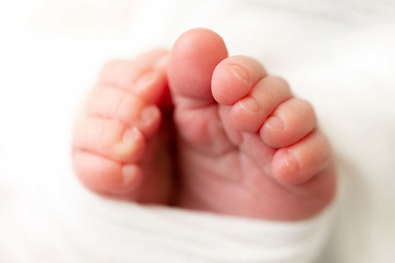 Close-up of tiny baby feet with delicate toes against white background.