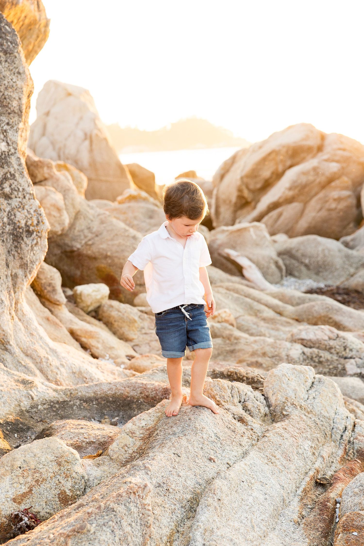 Child exploring rocky coastal terrain during golden hour.