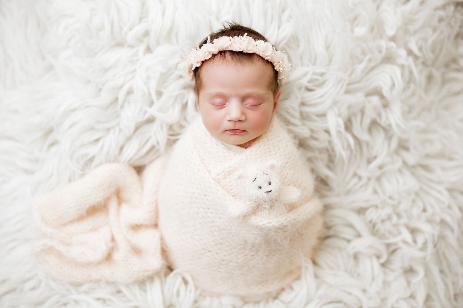 Newborn baby wrapped in soft white blankets lying on plush white fur background in multiple poses.