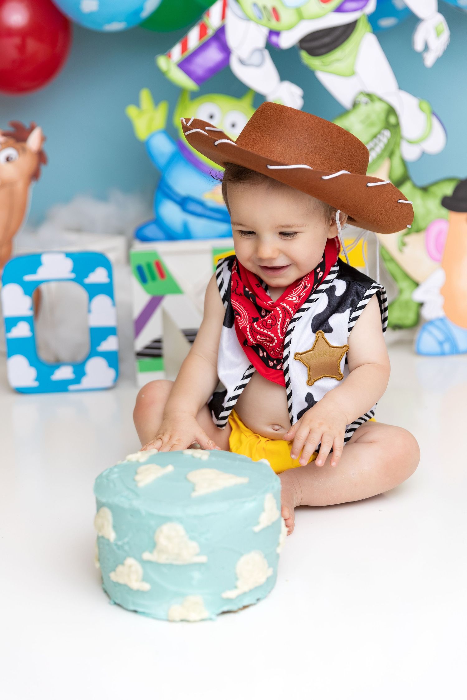 Western-themed cake smash setup with blue sky cake and colorful balloon backdrop.