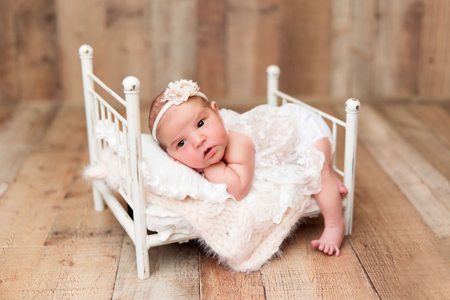 Small baby resting in vintage white wooden bed with lace details.