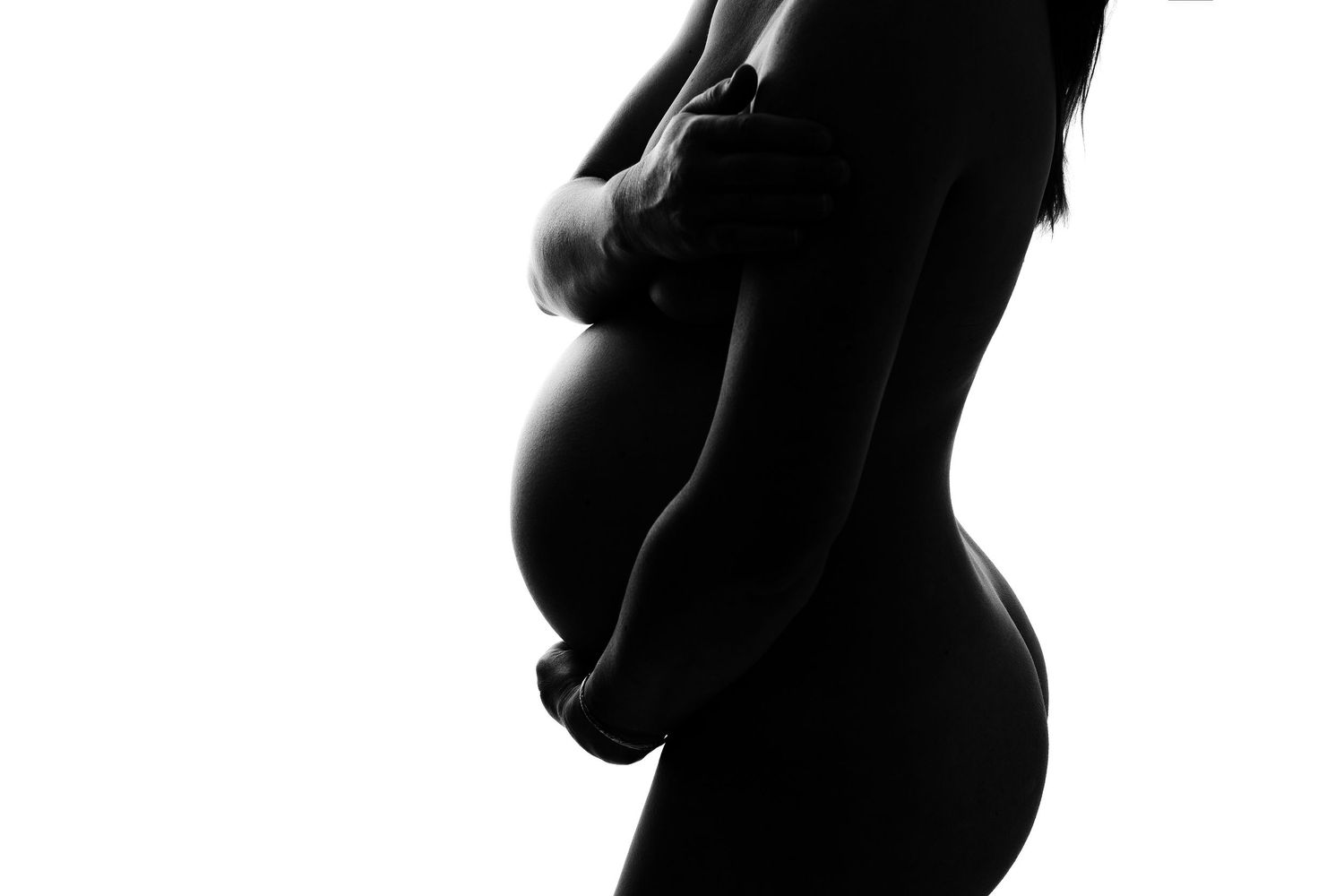Artistic black and white silhouette of pregnant figure against dark background.