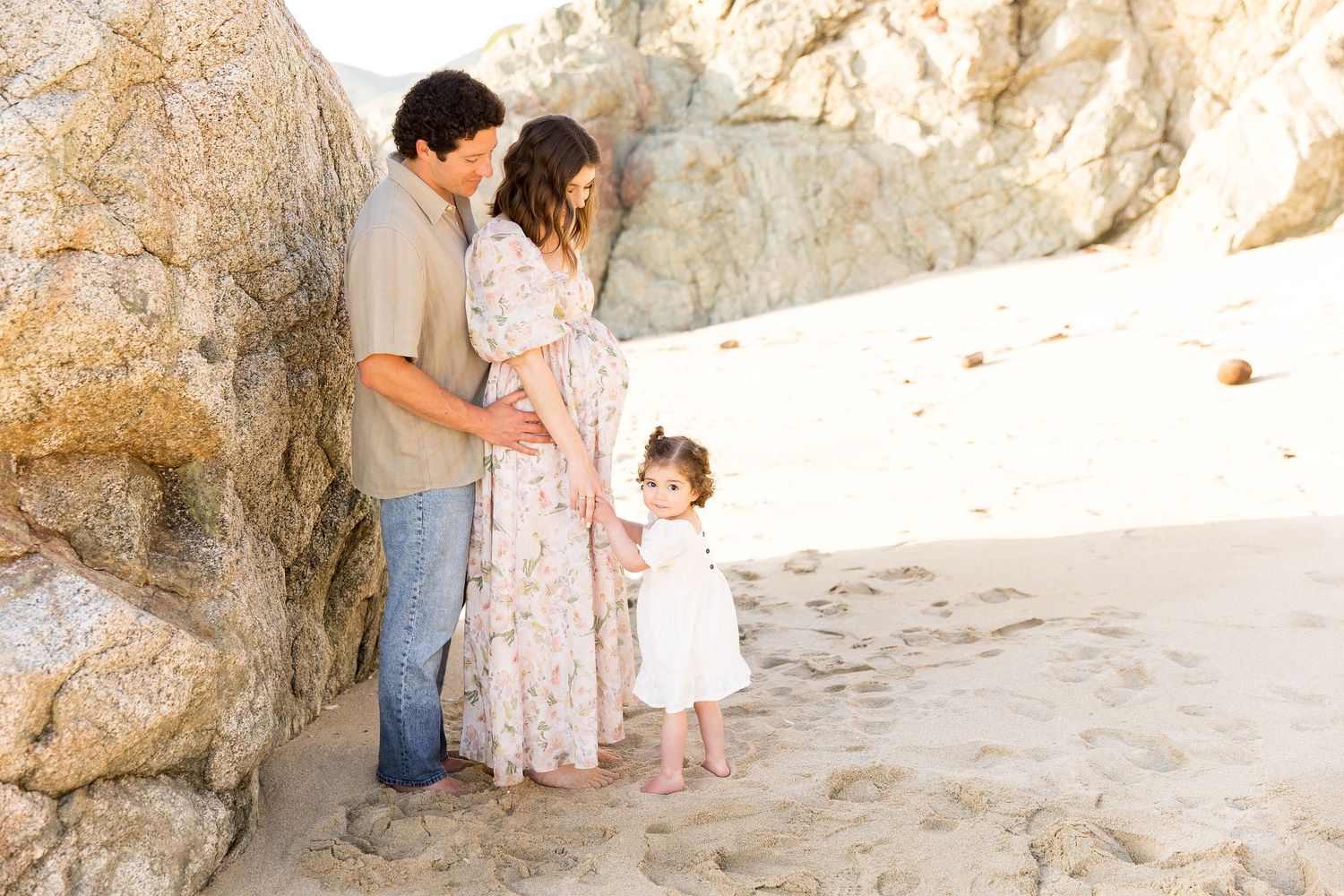 A family enjoying a sunny day at a rocky beach cove with cliffs in the background.