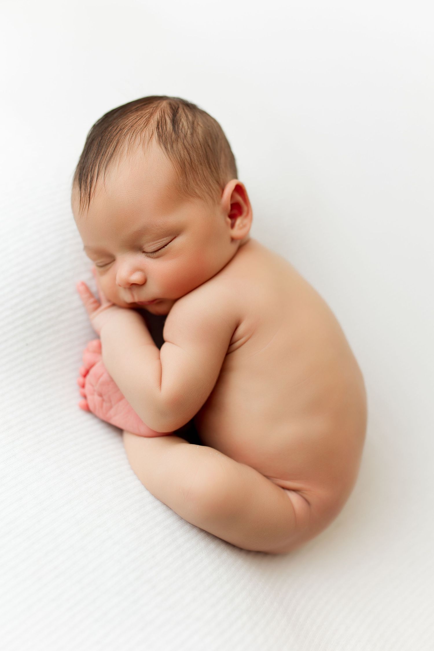Artistic black and white portrait of a sleeping newborn baby on white backdrop.