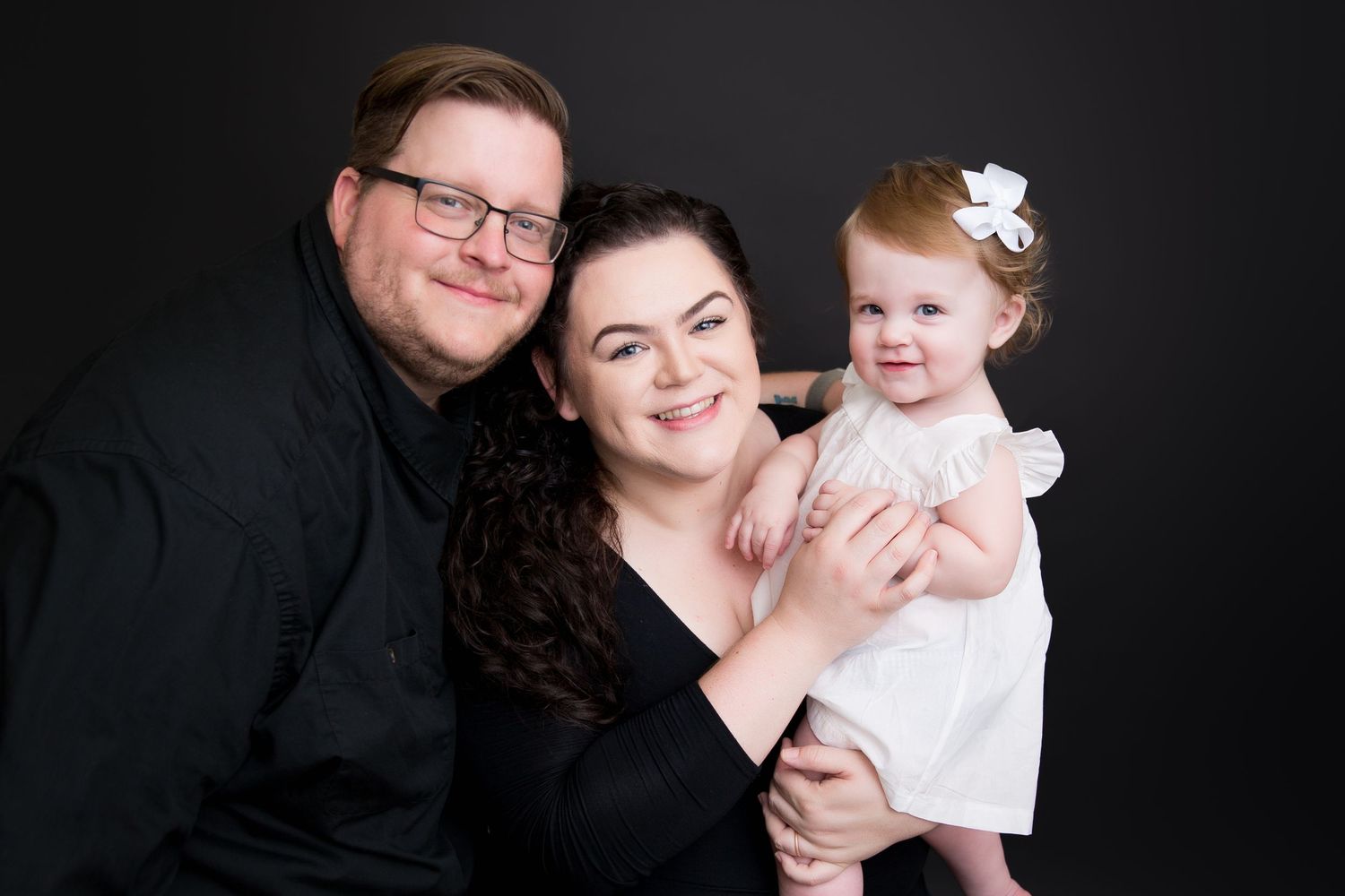 Professional family portrait against black background showing warm embraces.