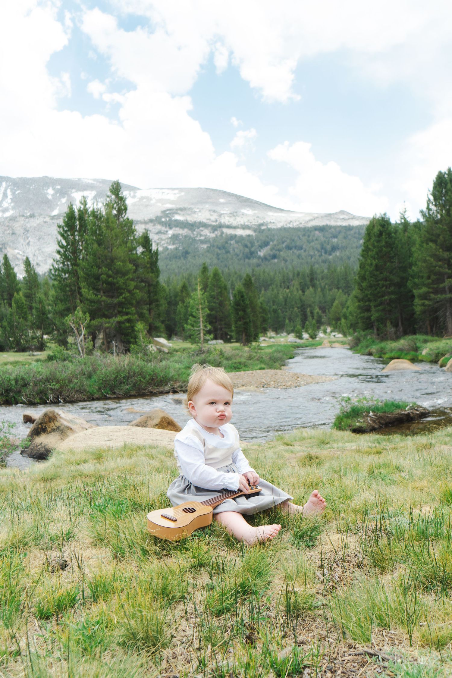 A young musician sits with a guitar in a mountain meadow beside a stream, sound of music inspired in Yosemite.
