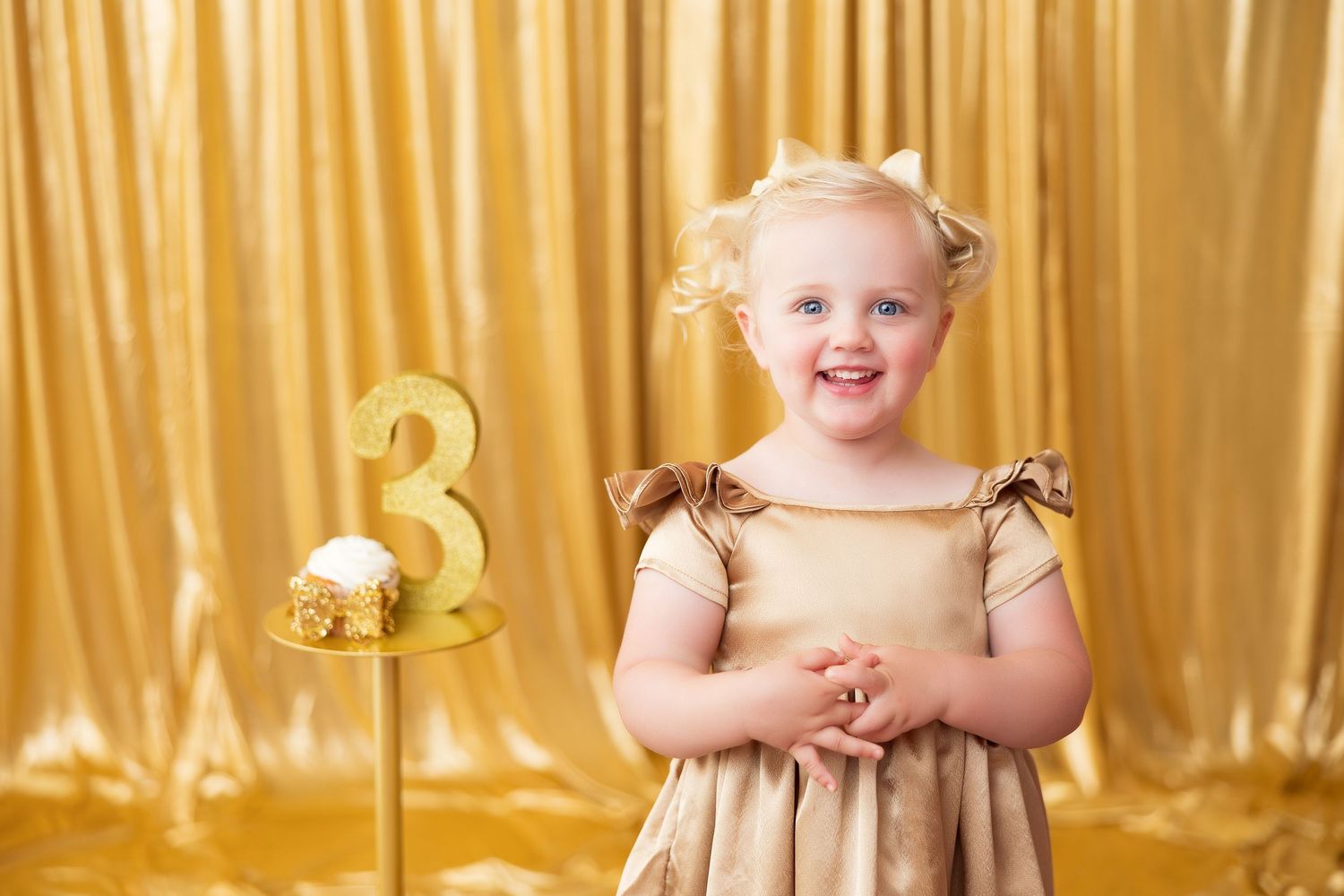 Two children in matching outfits laugh while standing in front of a gold curtain backdrop during a festive celebration.