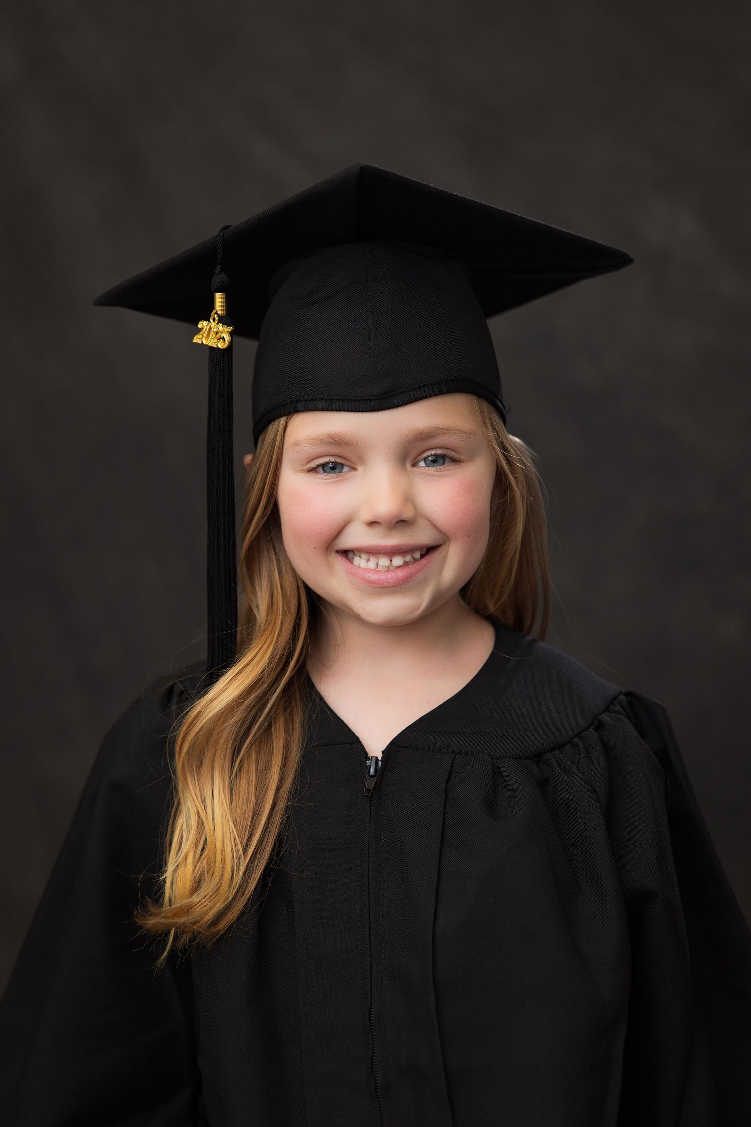 Portrait of a young student in a black graduation cap and gown against a dark background.