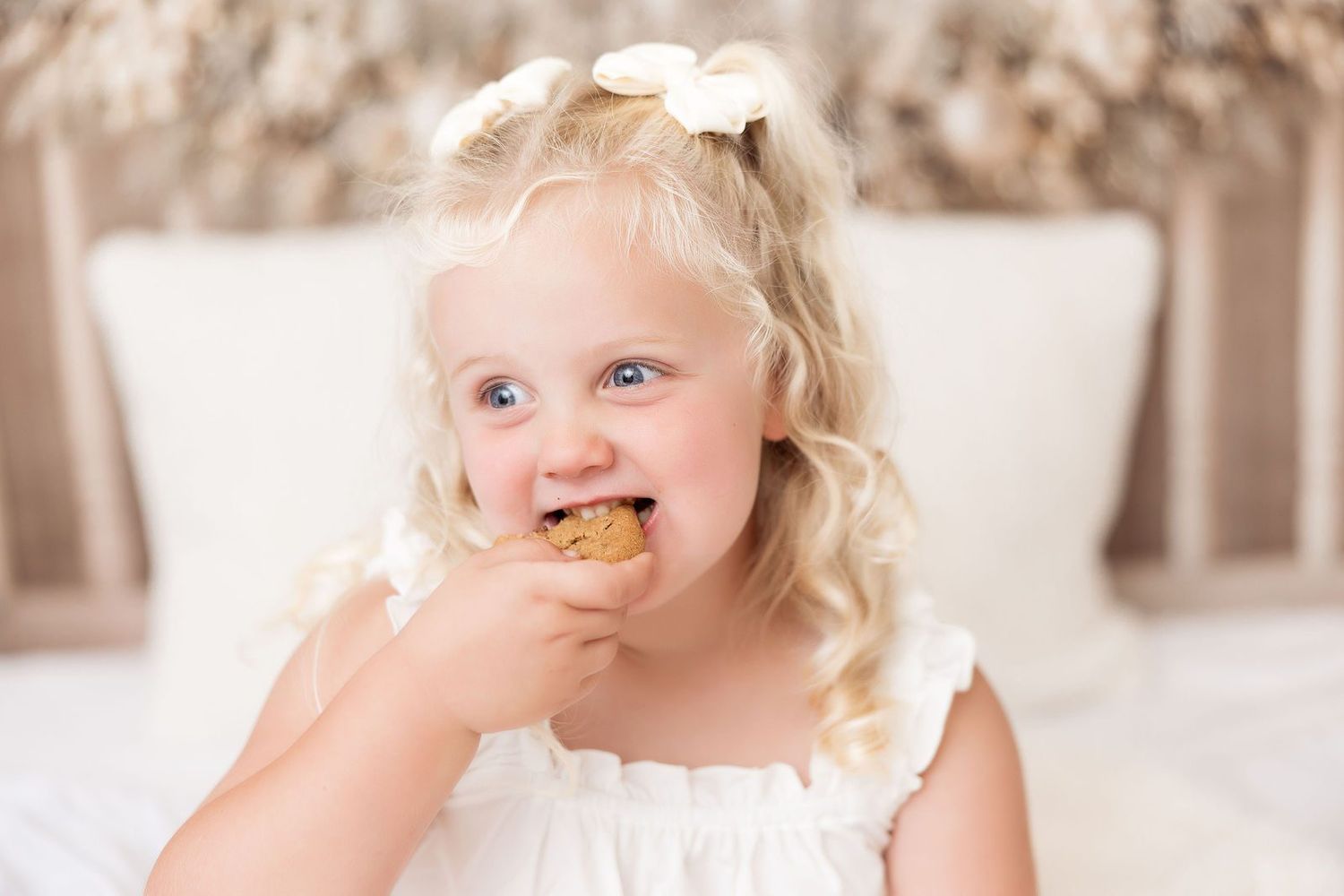 Little girl in white ruffle pajamas eating a cookie at a Milk and Cookies Christmas mini session in Monterey