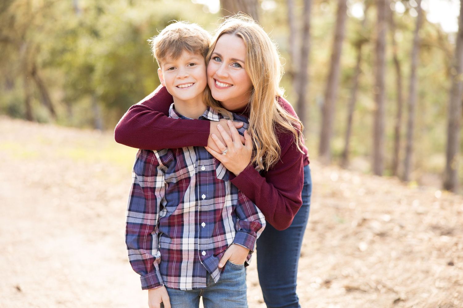 Two people share an affectionate moment while standing together on a forest path.