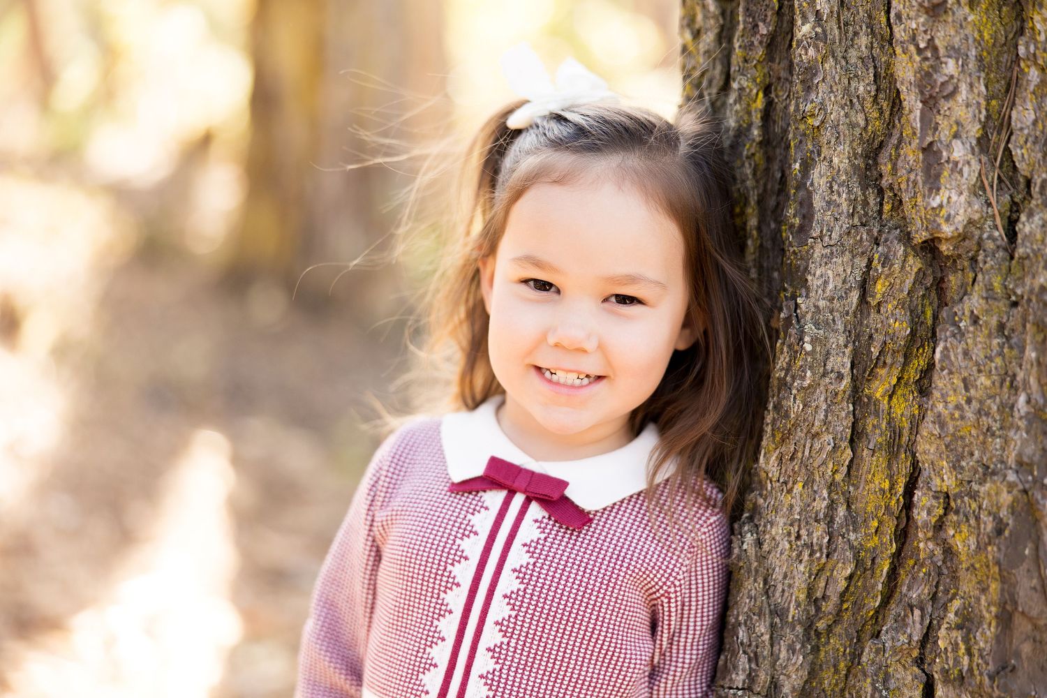 Young girl in checkered dress poses for closeup portrait against natural background.