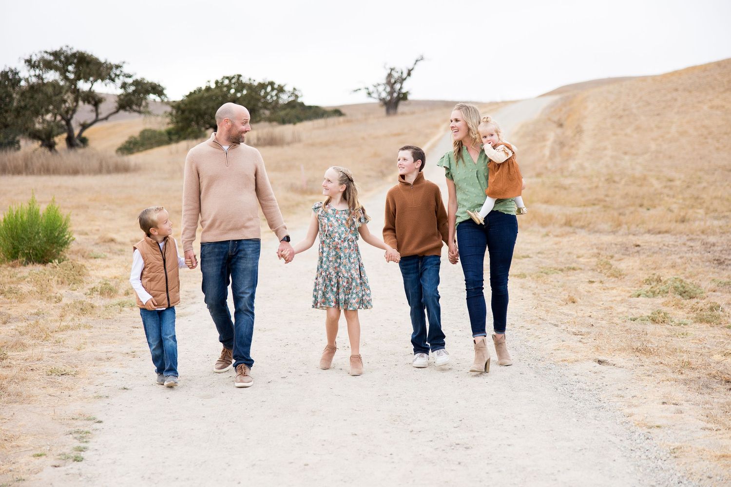 Family walking together hand-in-hand along a winding dirt path in a natural setting.
