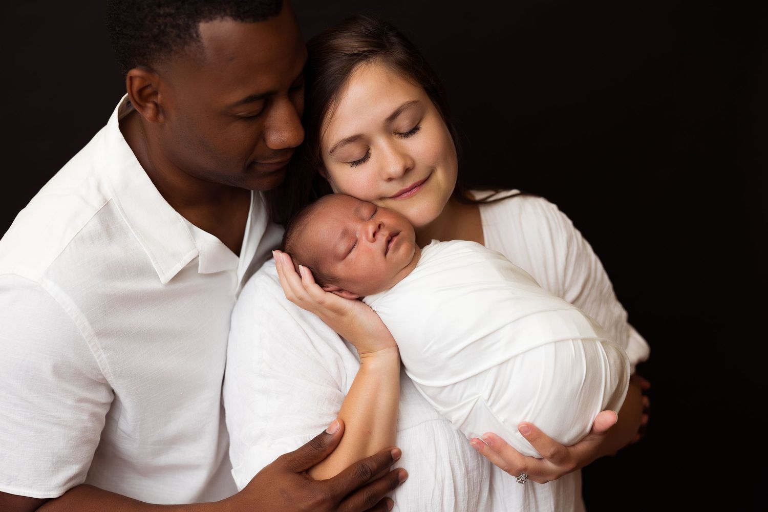 Intimate family portrait against dark background with everyone dressed in white.