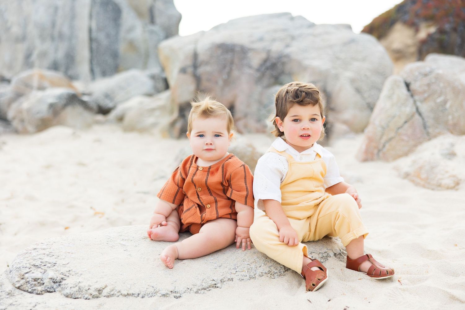 Family members relaxing on sandy beach with large rocks in background.