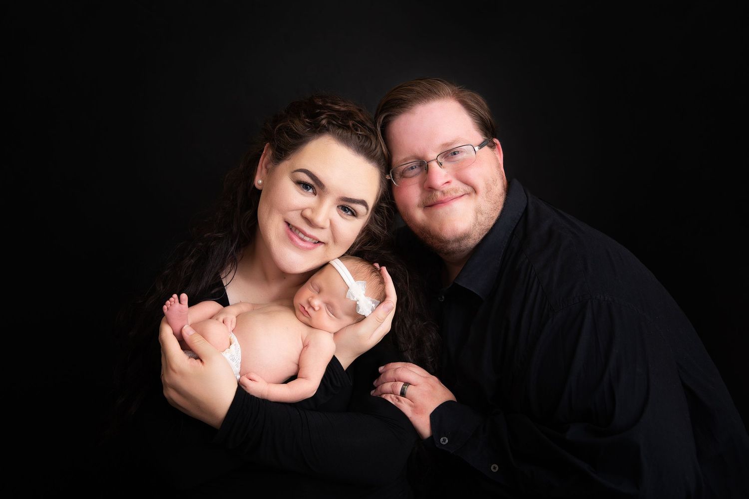 A professional studio portrait against black background featuring a newborn.
