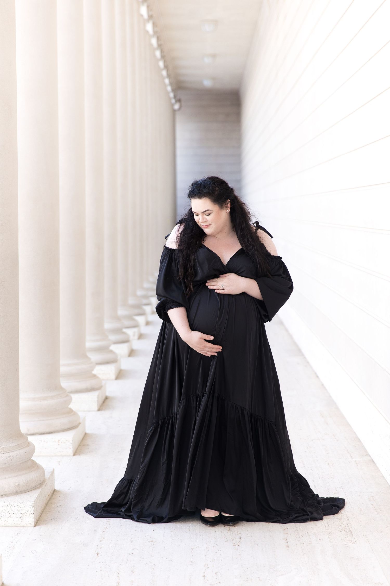 Graceful pose in flowing black dress amid white architectural columns.