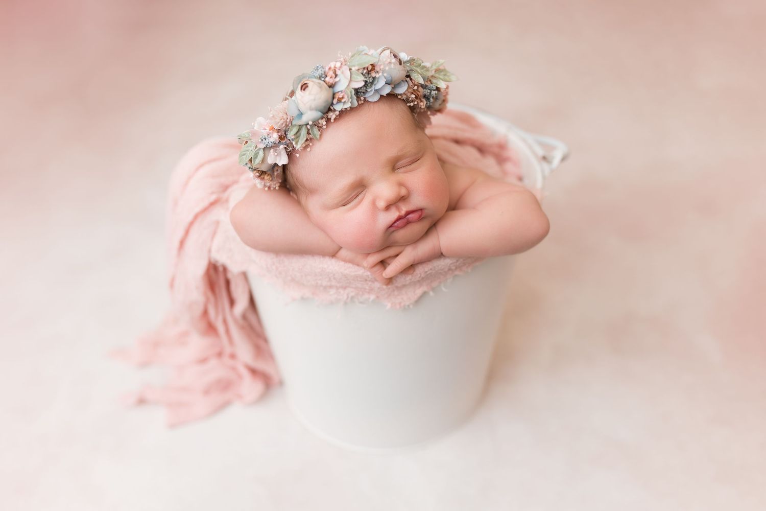 Peaceful newborn portrait with floral crown on delicate pink background.