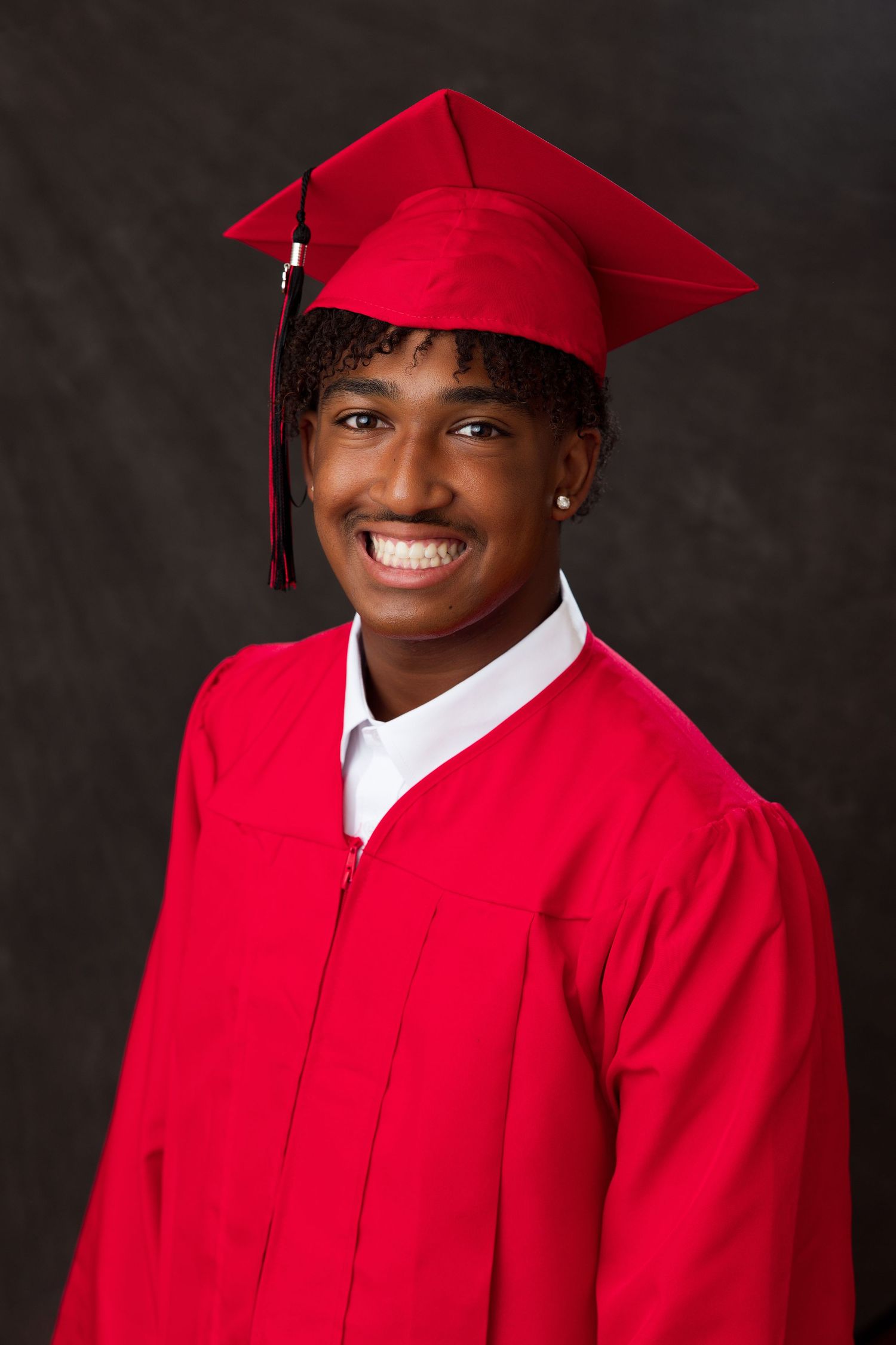 Smiling young man in red graduation cap and gown posing for a portrait photo.