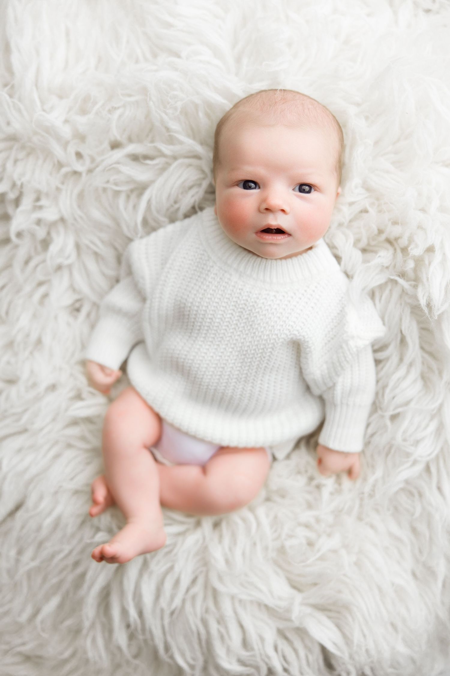 Baby wearing white sweater lying on fluffy white rug in progression of different poses.