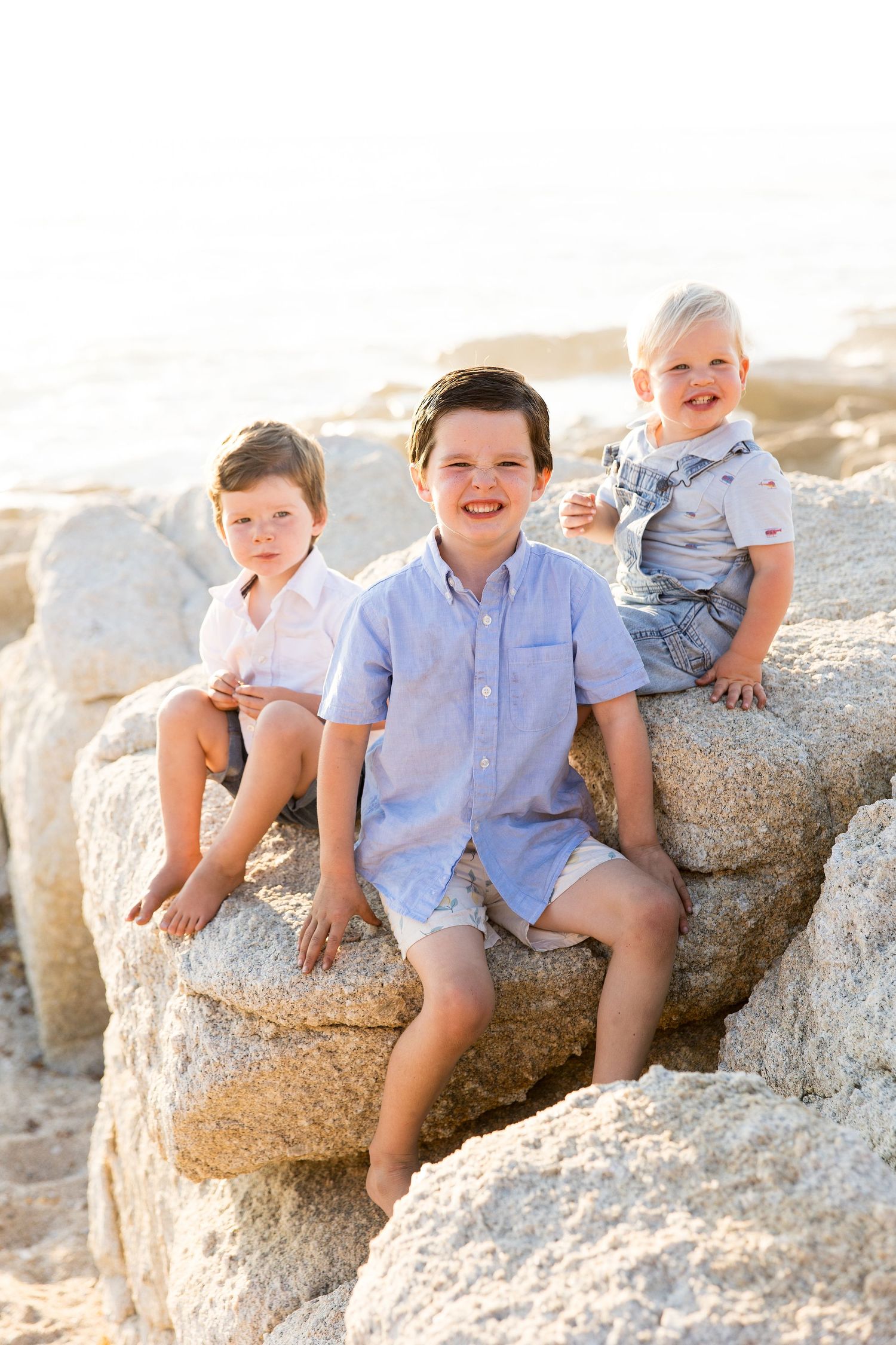 Kids in light blue shirts lounging on rocky beach formation during sunset photoshoot.