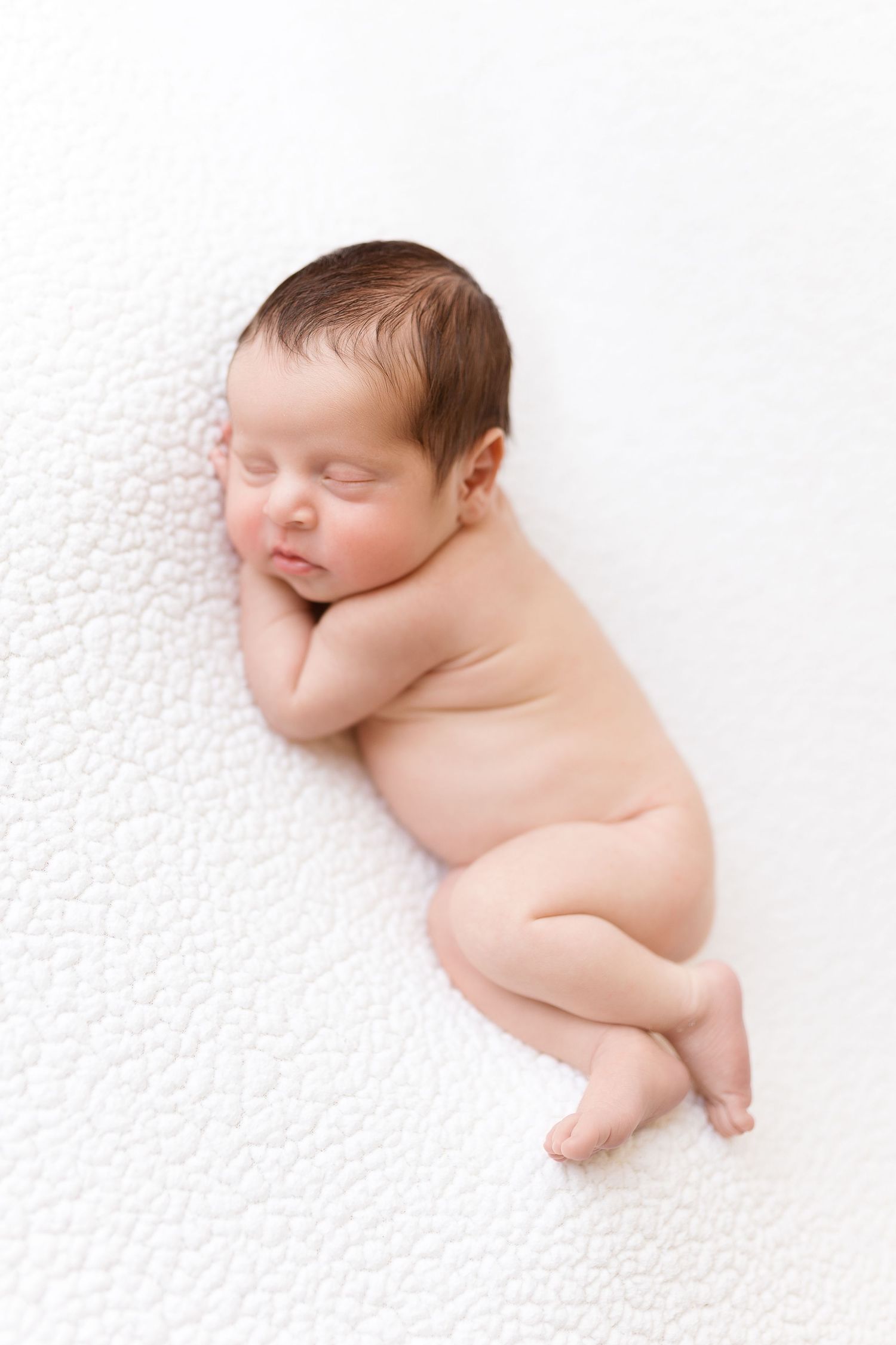 Sleeping newborn rests on textured white background in artistic pose.