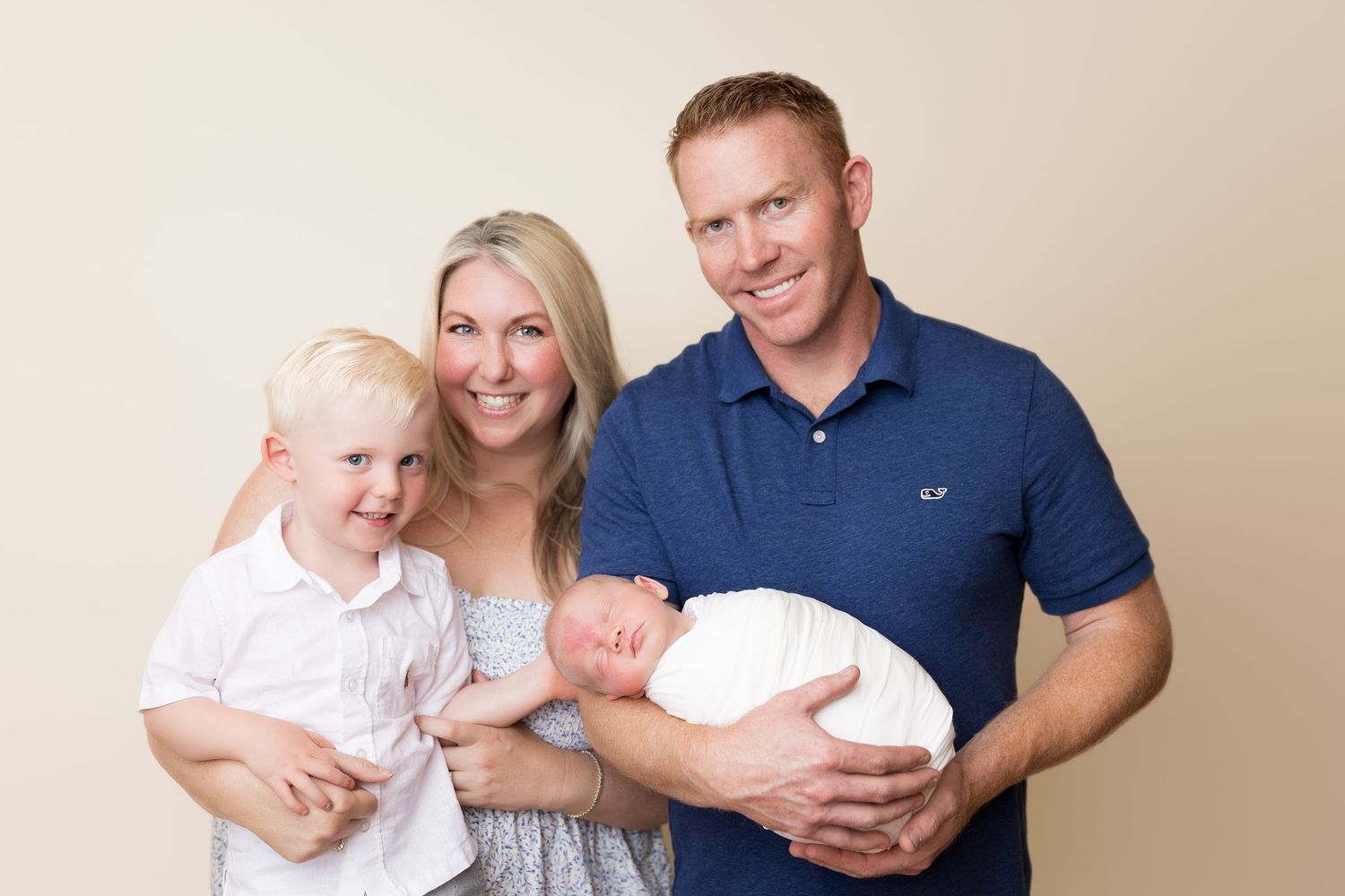 Family portrait with newborn baby against neutral background.