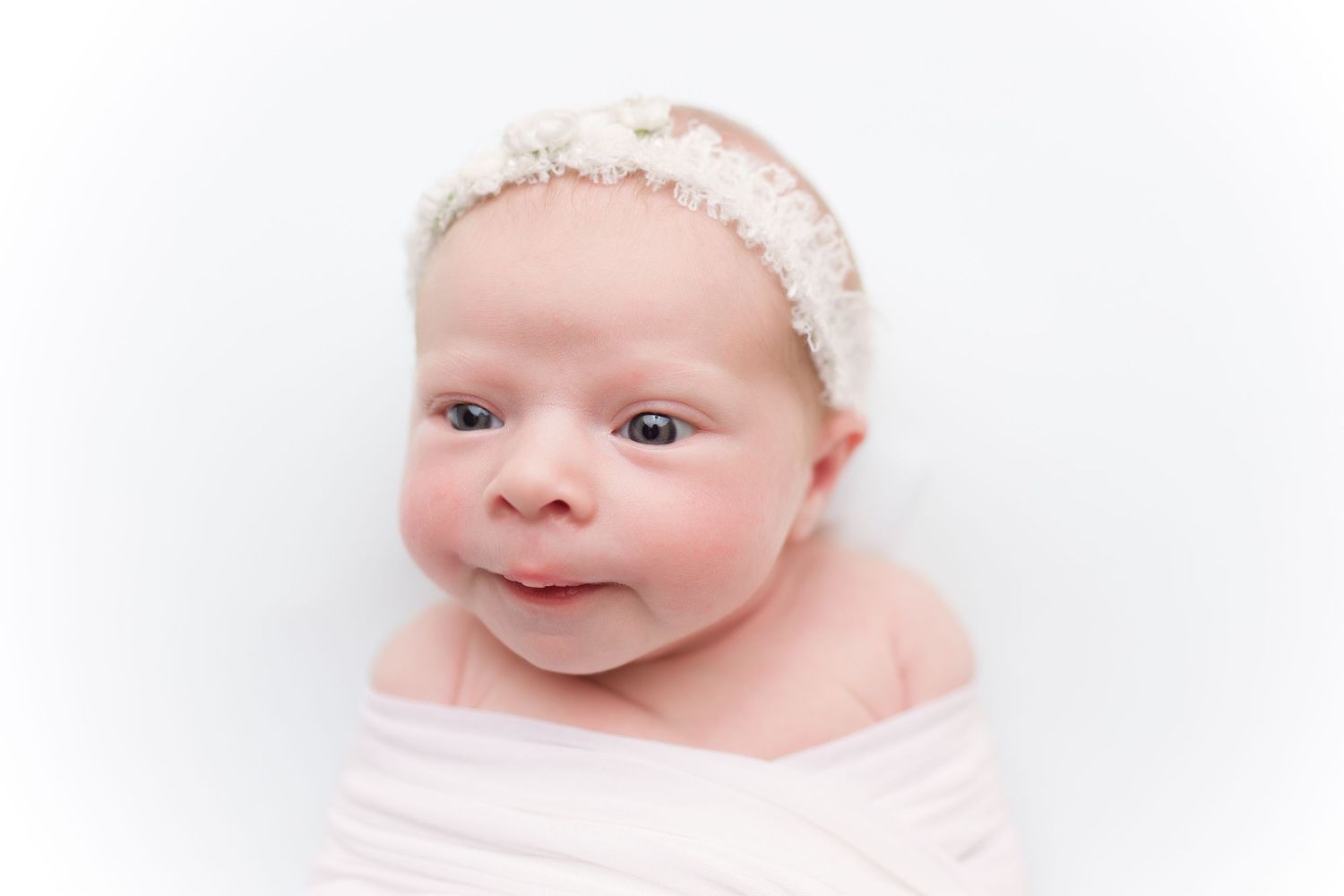 Newborn baby wearing lace headband against minimalist white setting.