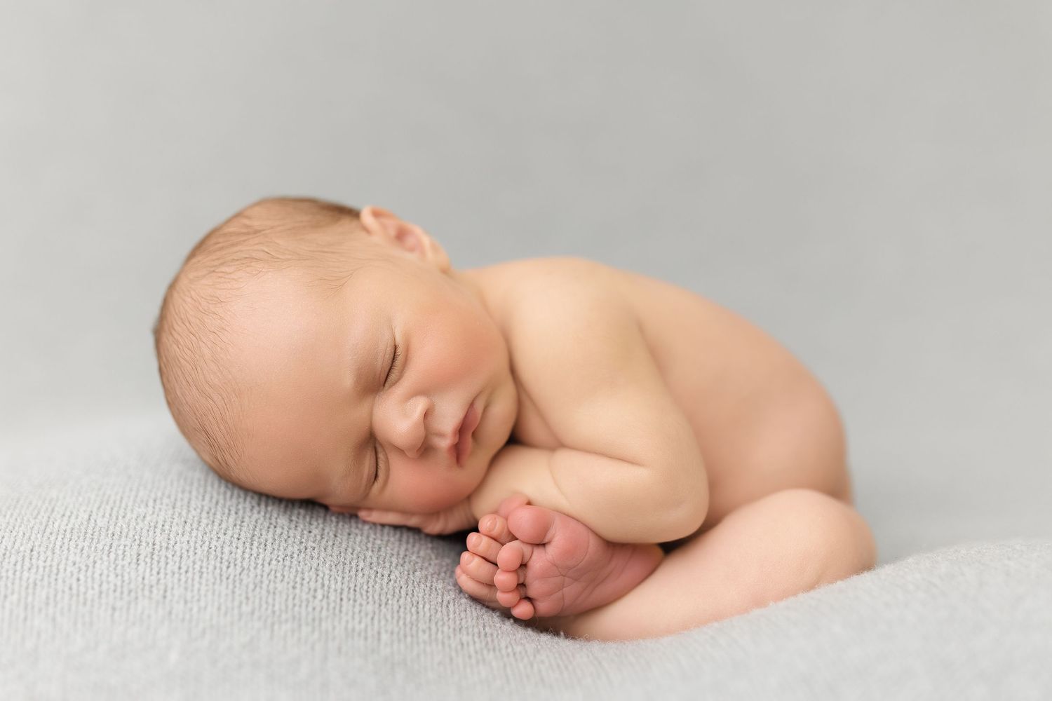 A sleeping newborn baby lies peacefully on soft white fabric in a minimalist photography style.