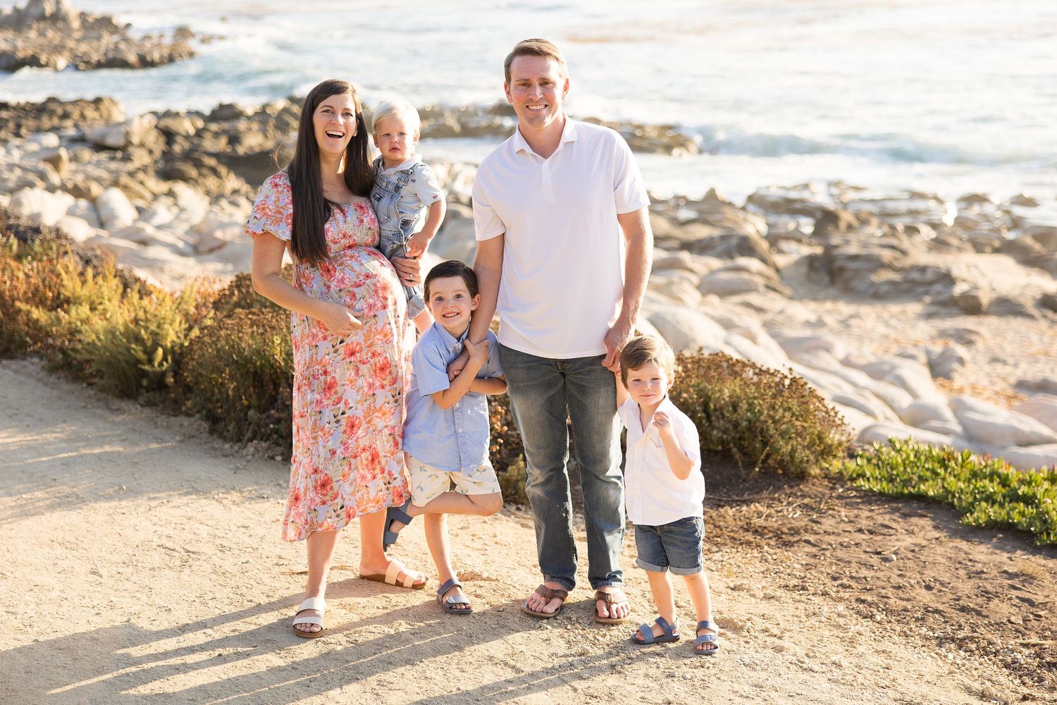 Family enjoying a sunset photo session on rocky coastal cliffs in coordinated outfits.