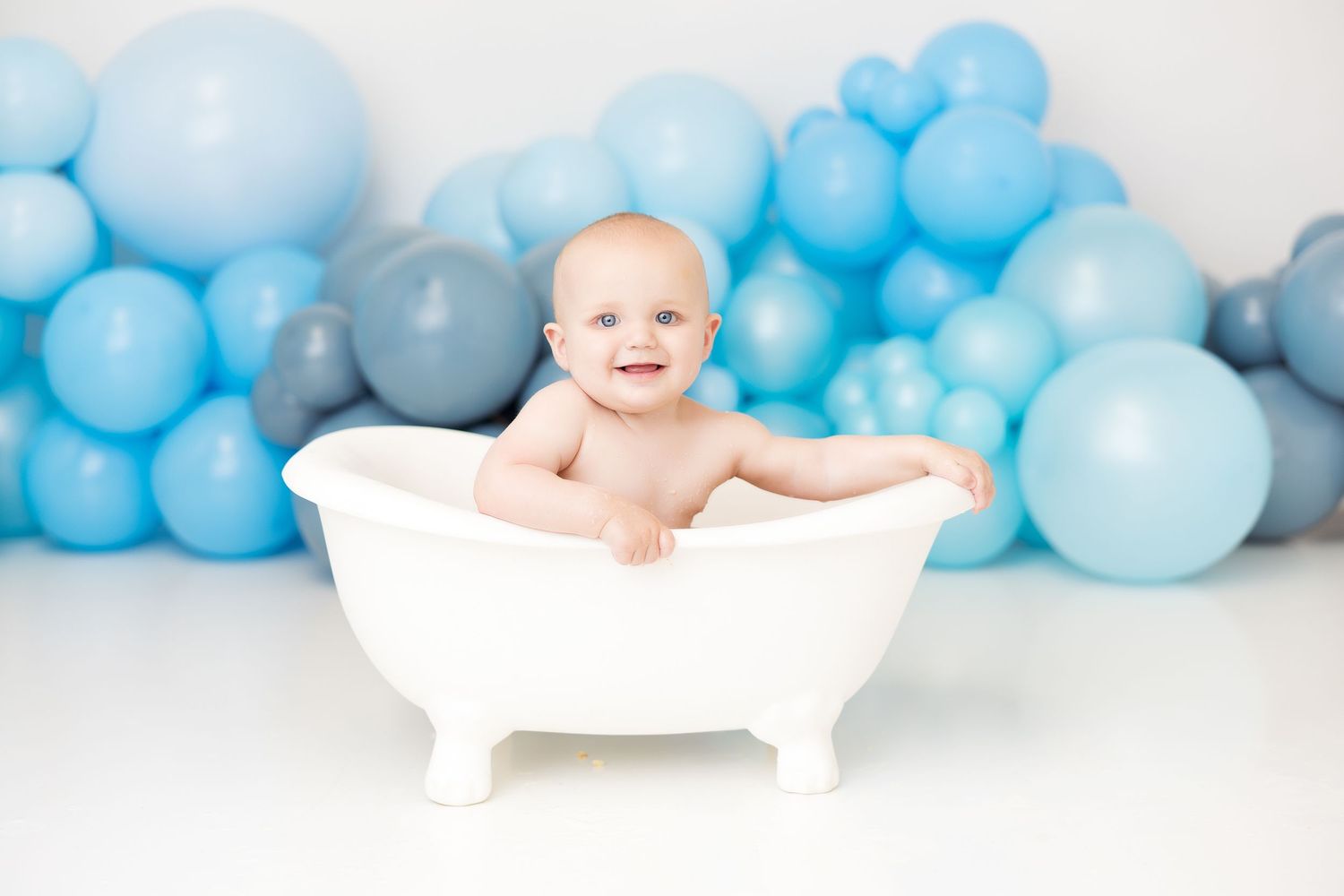White bathtub setup with blue balloon garland background for baby photography session.