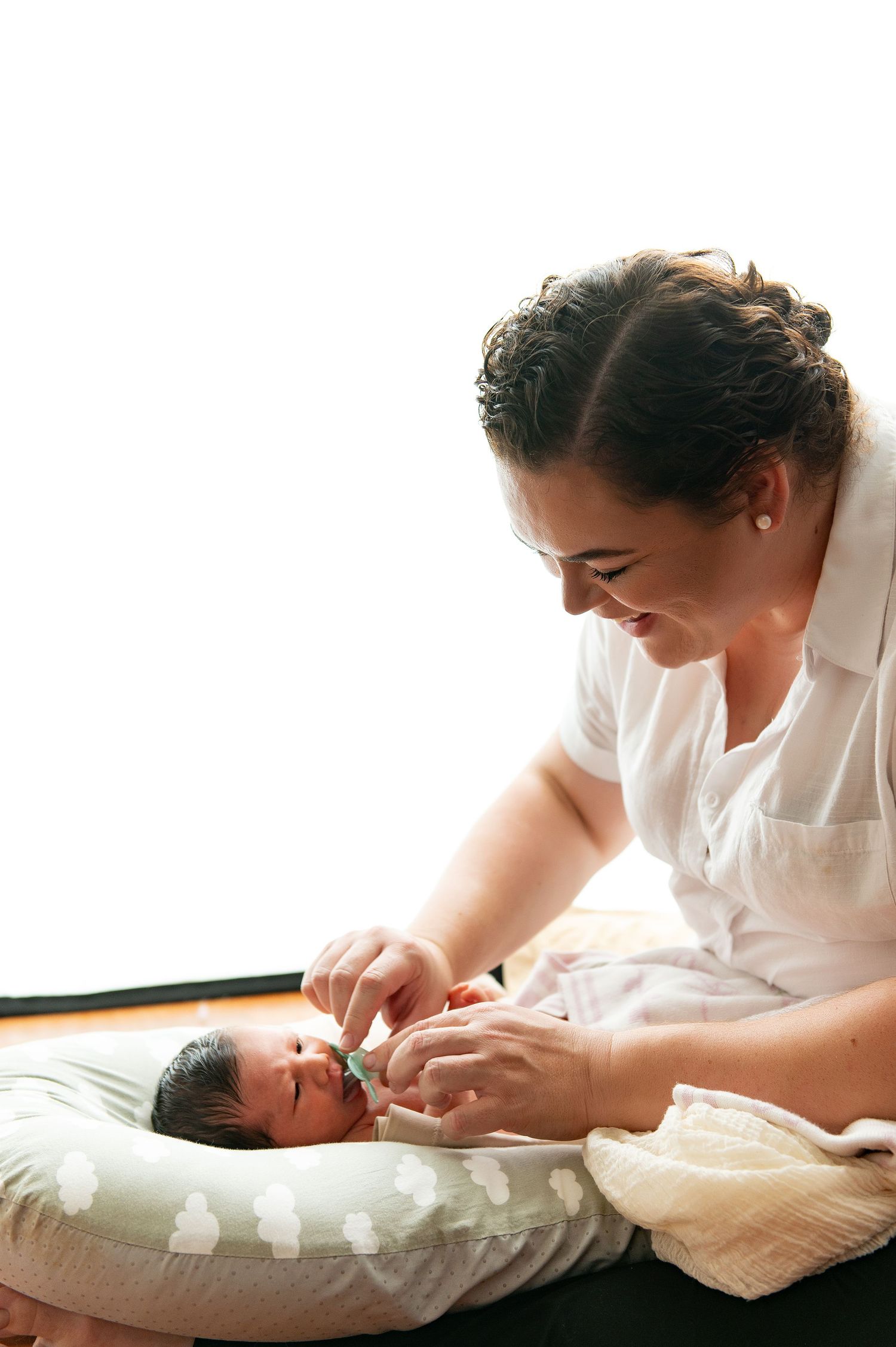 A tender moment between parent and newborn baby lying on a nursing pillow in natural light.