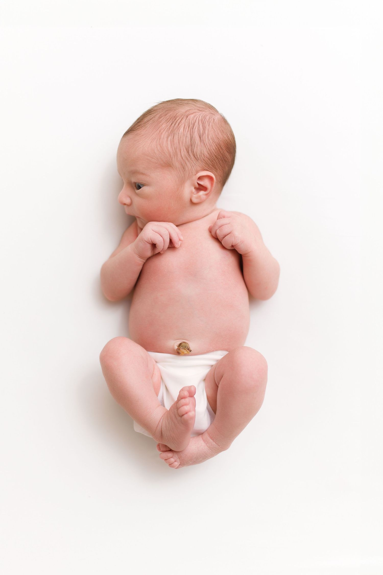 Newborn baby in diaper lying on white background looking to the side.
