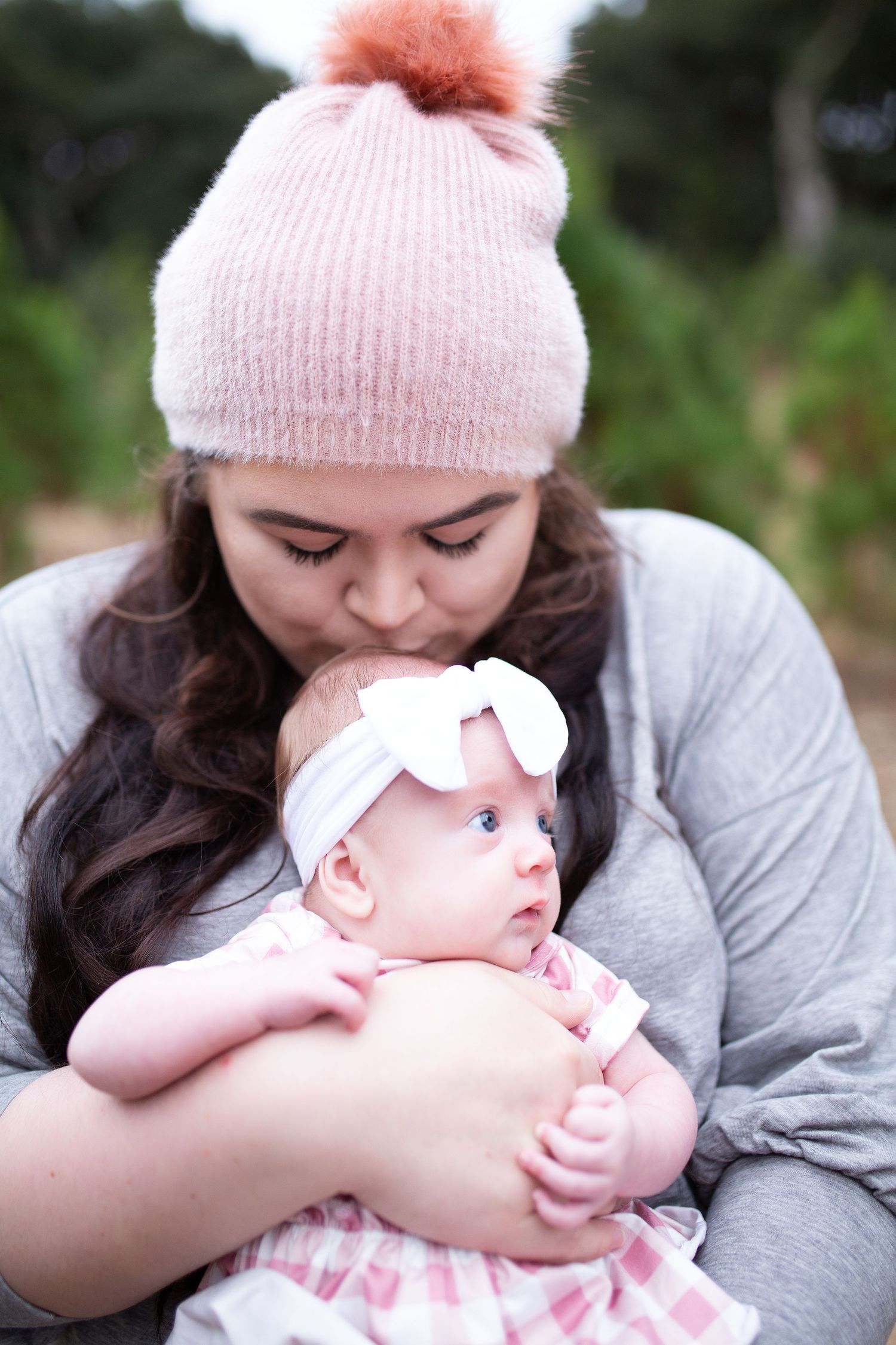 Tender moment between parent and baby wearing pink knit hat during outdoor photography.