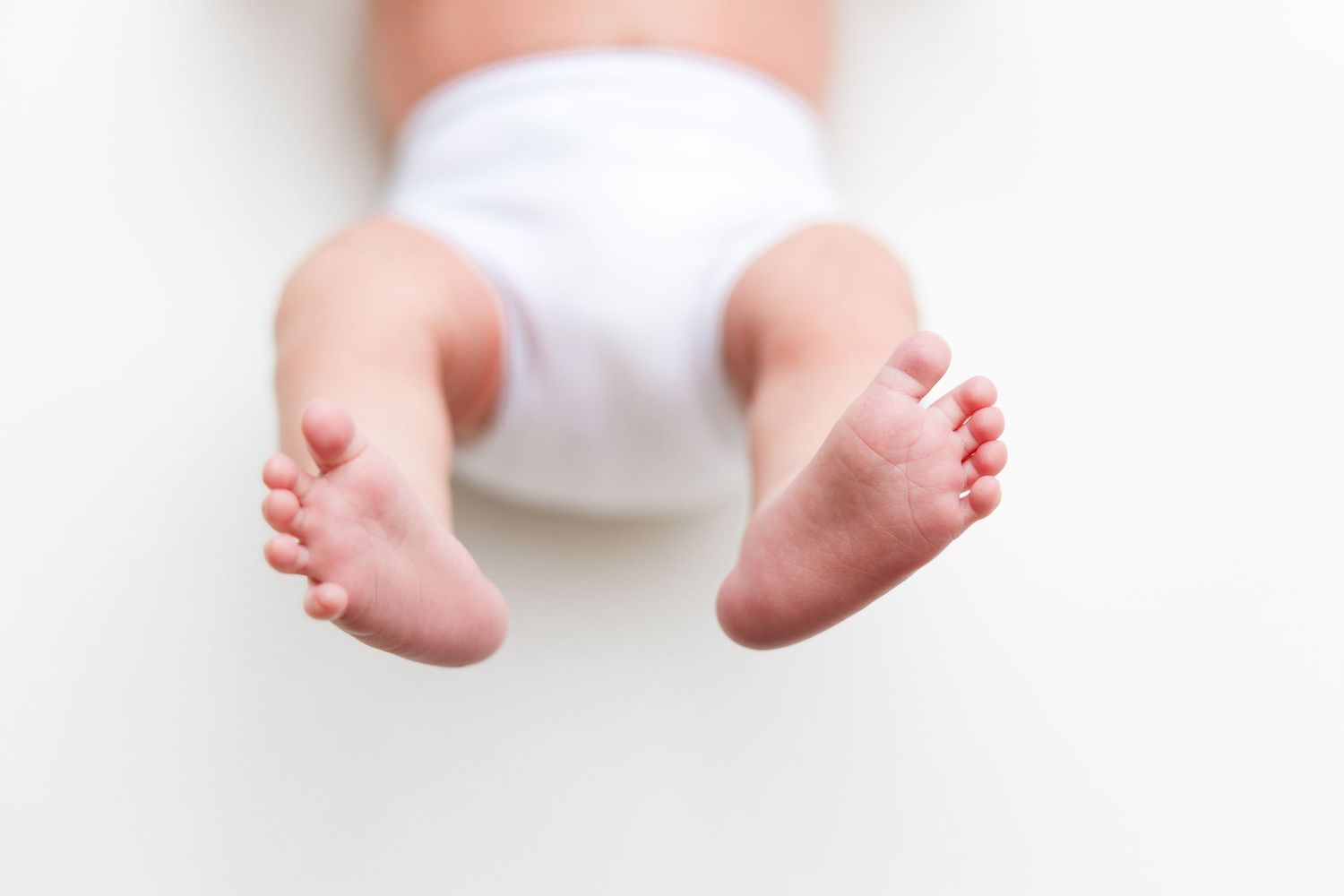 Close up of tiny baby feet against white background.