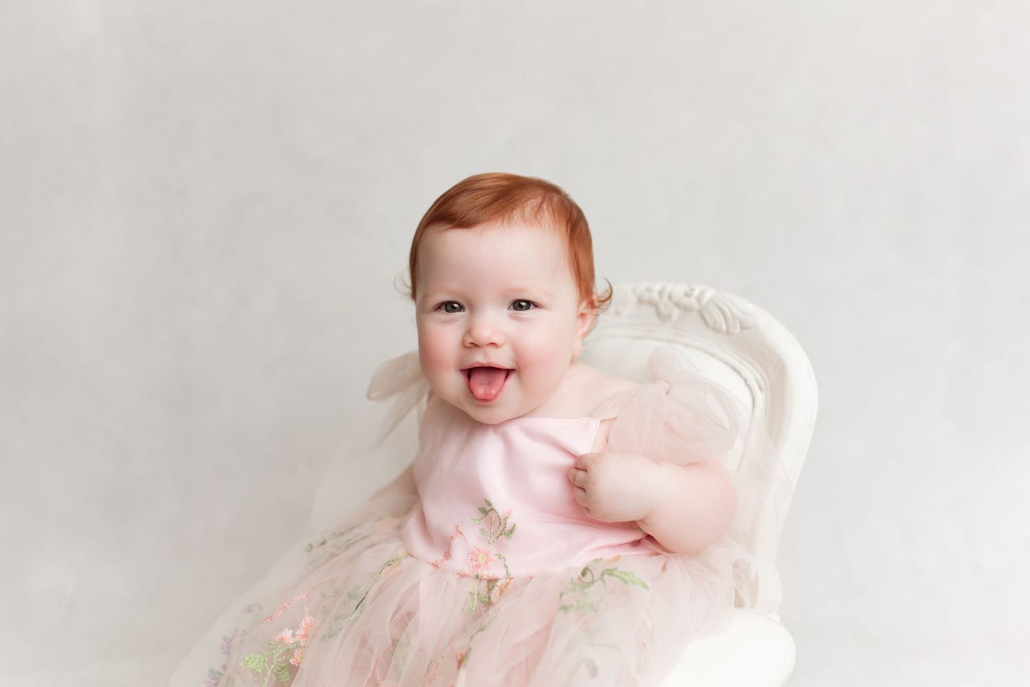 Portrait of a joyful baby wearing a pink dress with bow detail against white background.