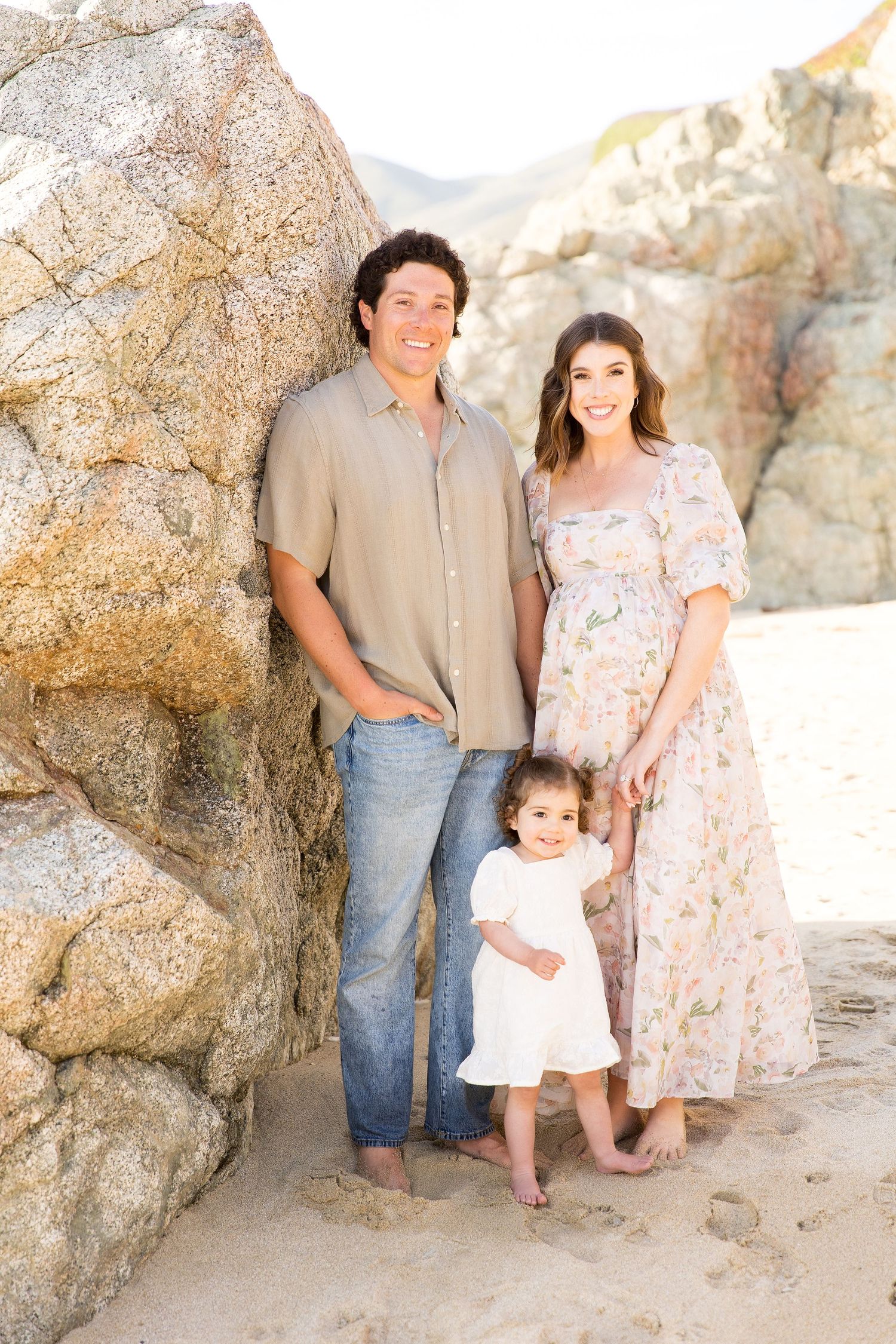 A family poses together near large rock formations on a sandy beach.