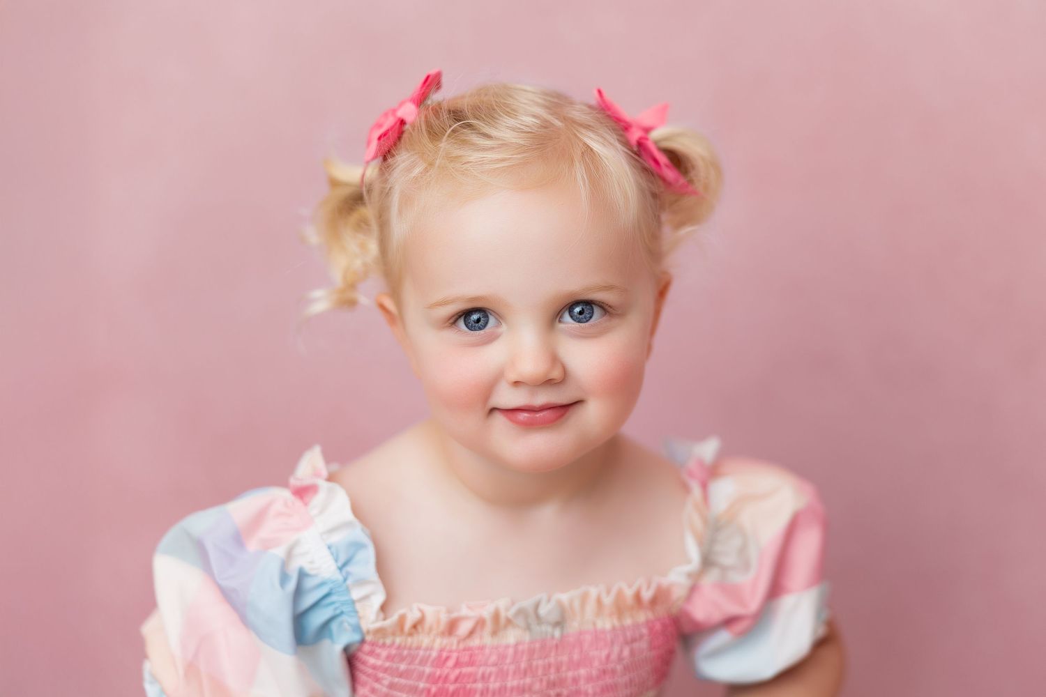A sweet portrait of a toddler in pink against a rosy background with delicate hair bows.