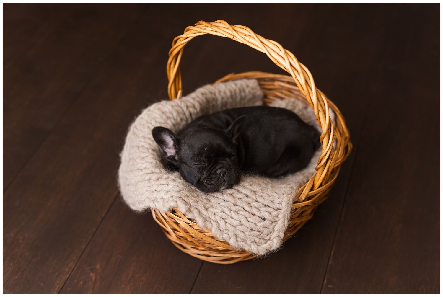 Black kitten sleeping peacefully in a woven wicker basket with white knitted blanket.