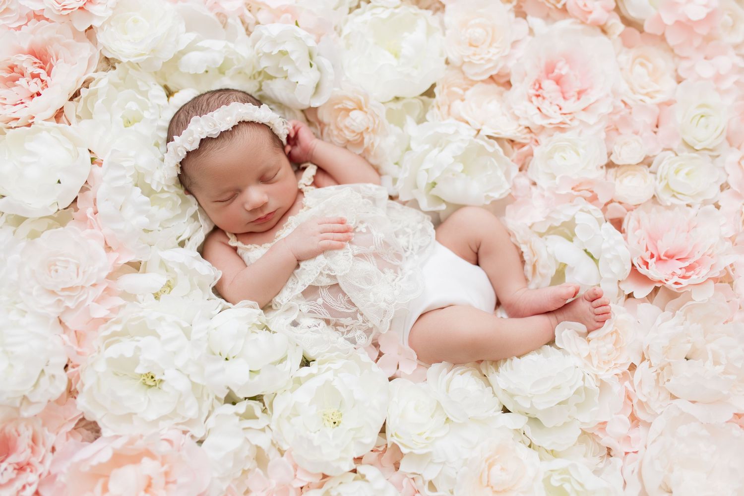 Sleeping baby with lace headband on bed of pink and white roses.