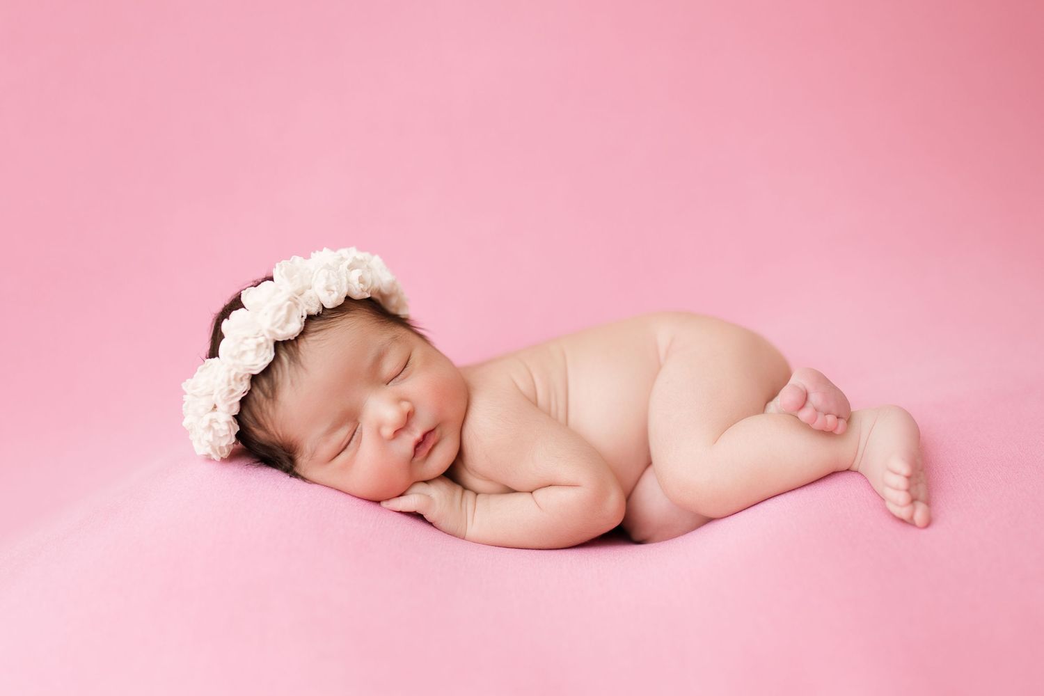 Newborn photography on pink background with floral headpiece.