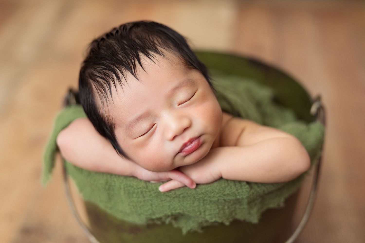 Peacefully sleeping newborn nestled in green bowl on wooden surface.