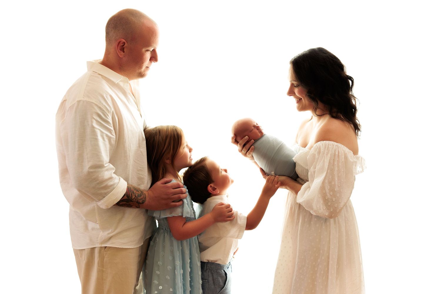 Family portrait session in coordinating white outfits against neutral background at photo studio.