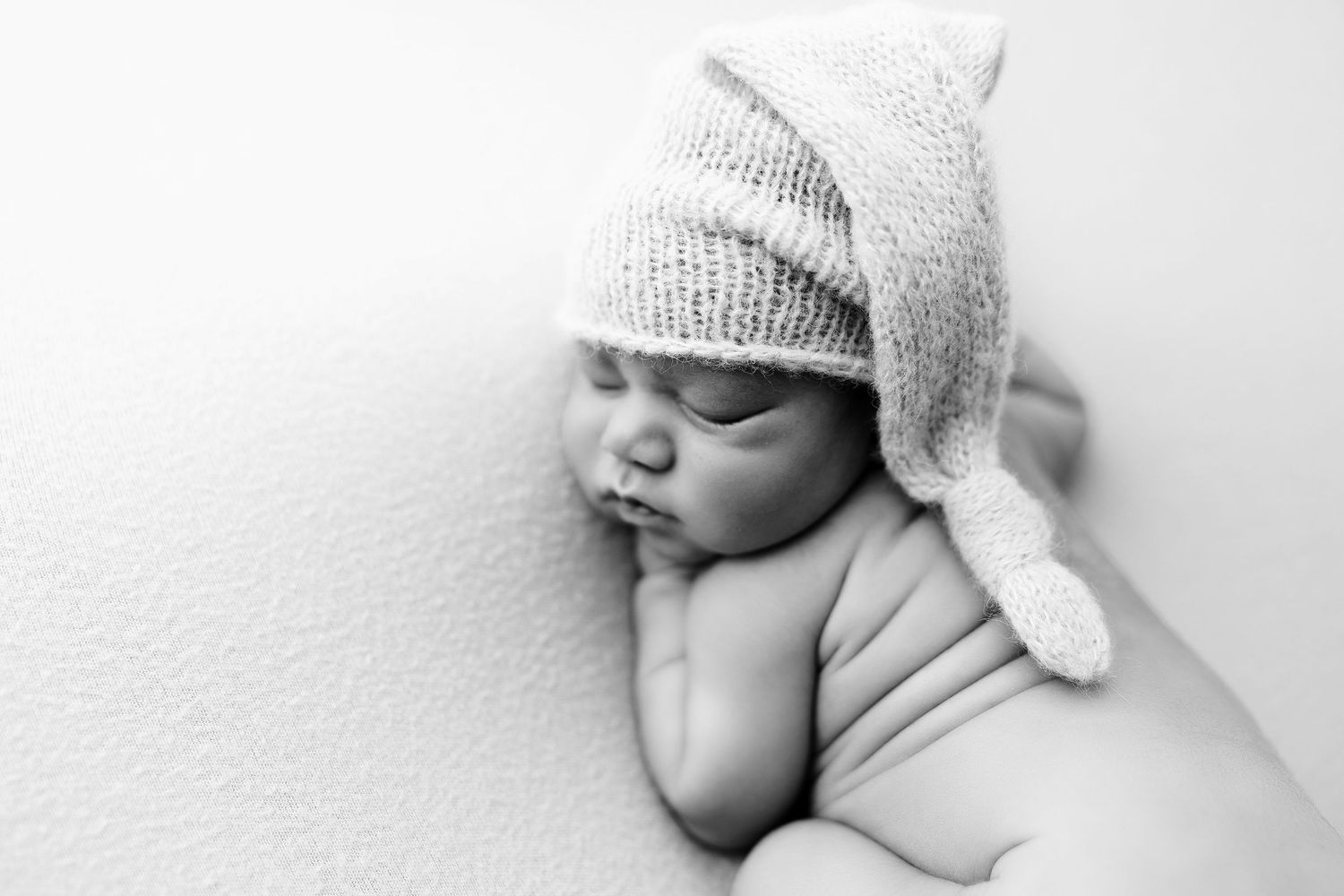 Newborn baby wearing a knit hat sleeps peacefully in black and white portrait.