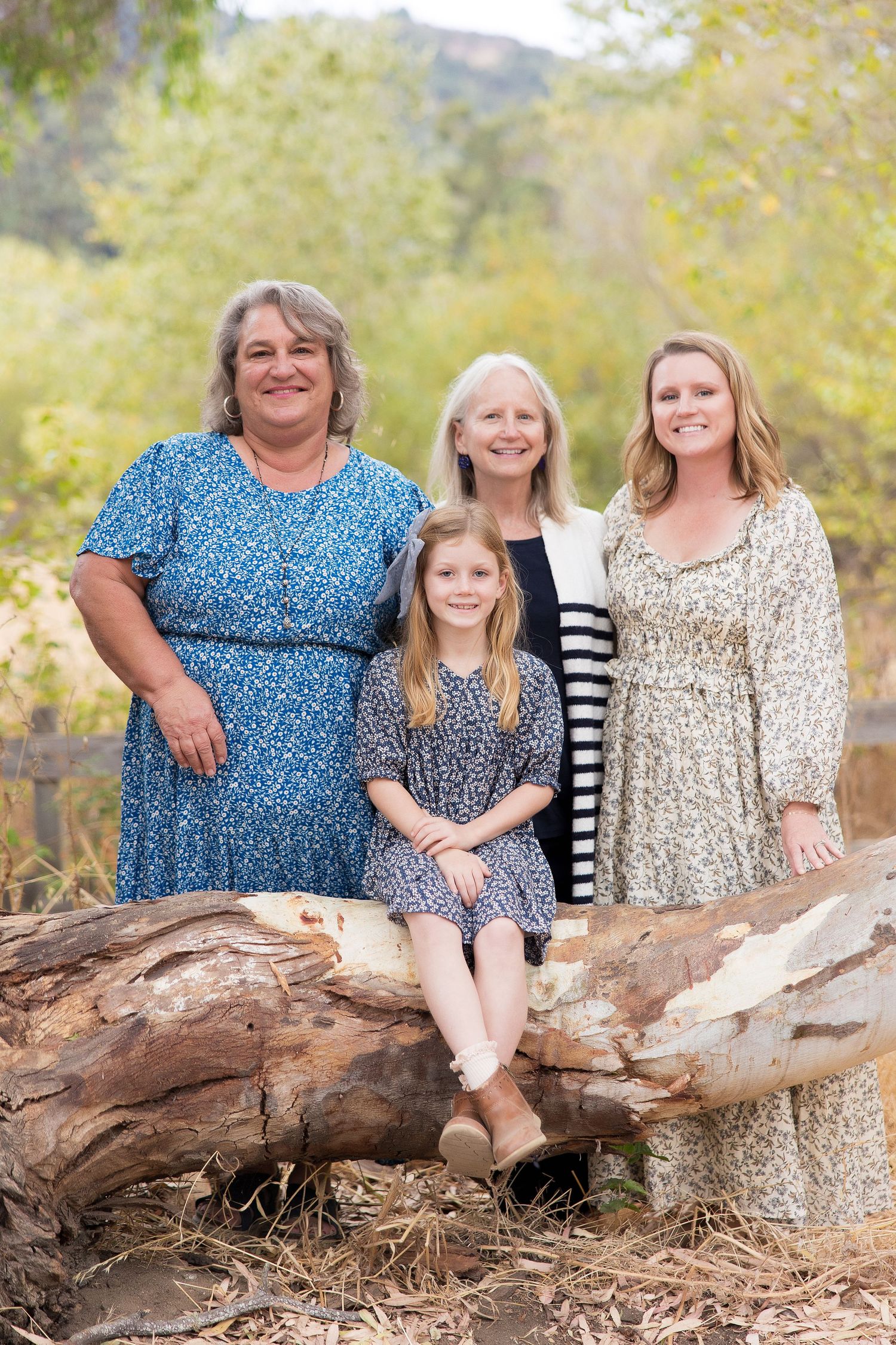 Three generations of family members pose together outdoors on a fallen log in Carmel Vallery.