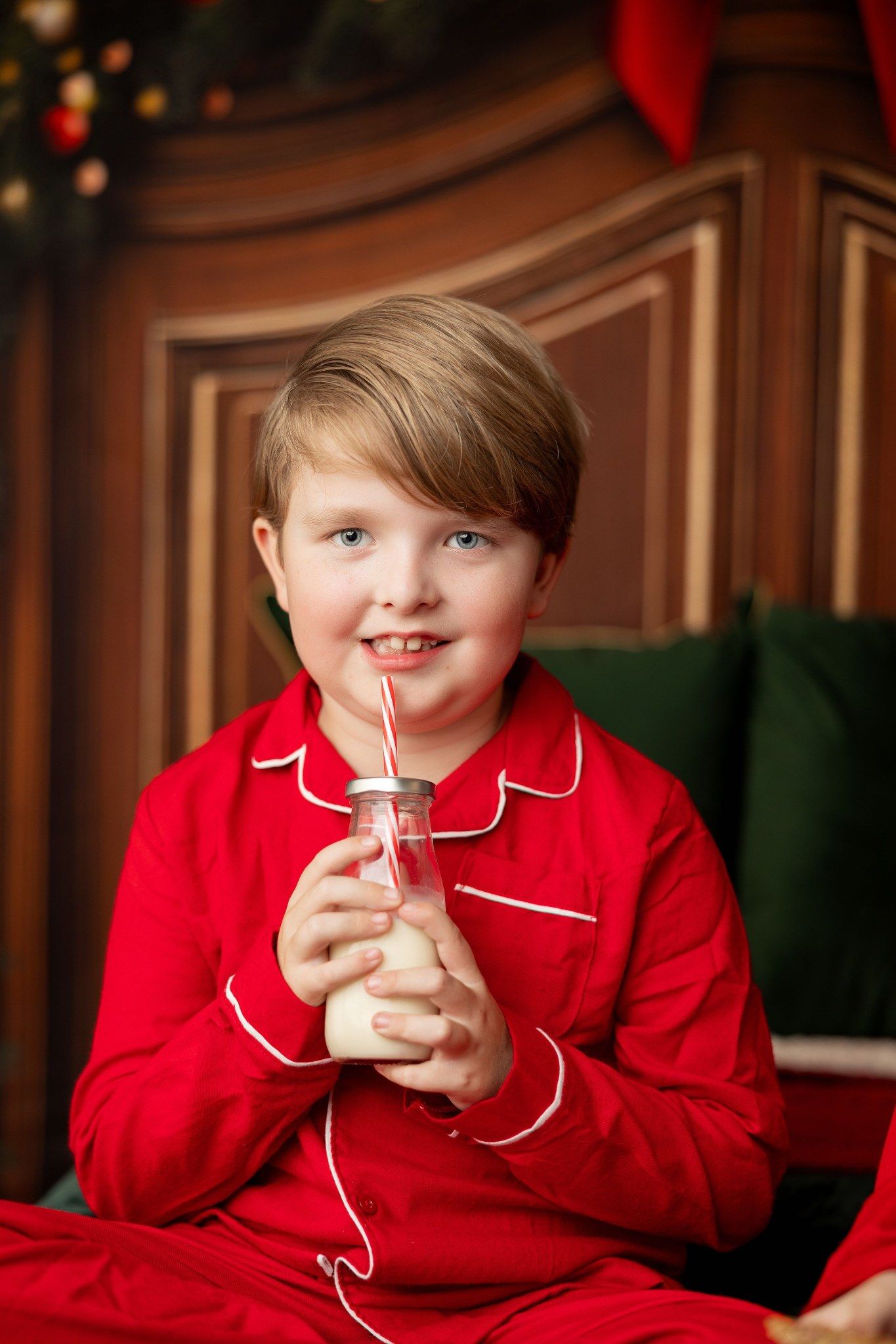 Boy in red Christmas pajamas holding a jar of milk with a straw at a holiday mini session in Pacific Grove