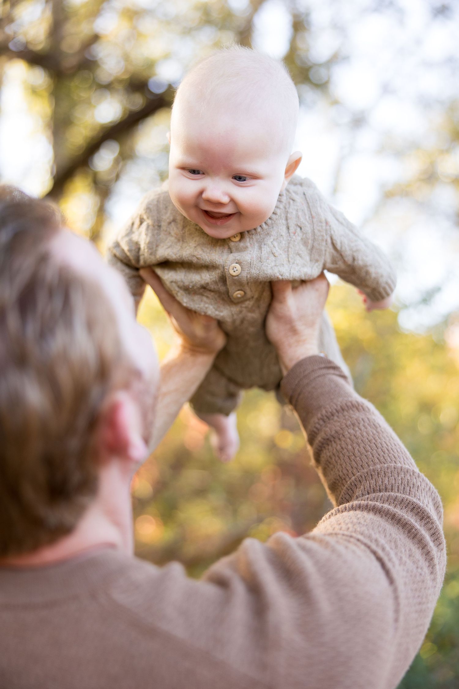 Playful family moment in the forest with a baby wearing a knit sweater.