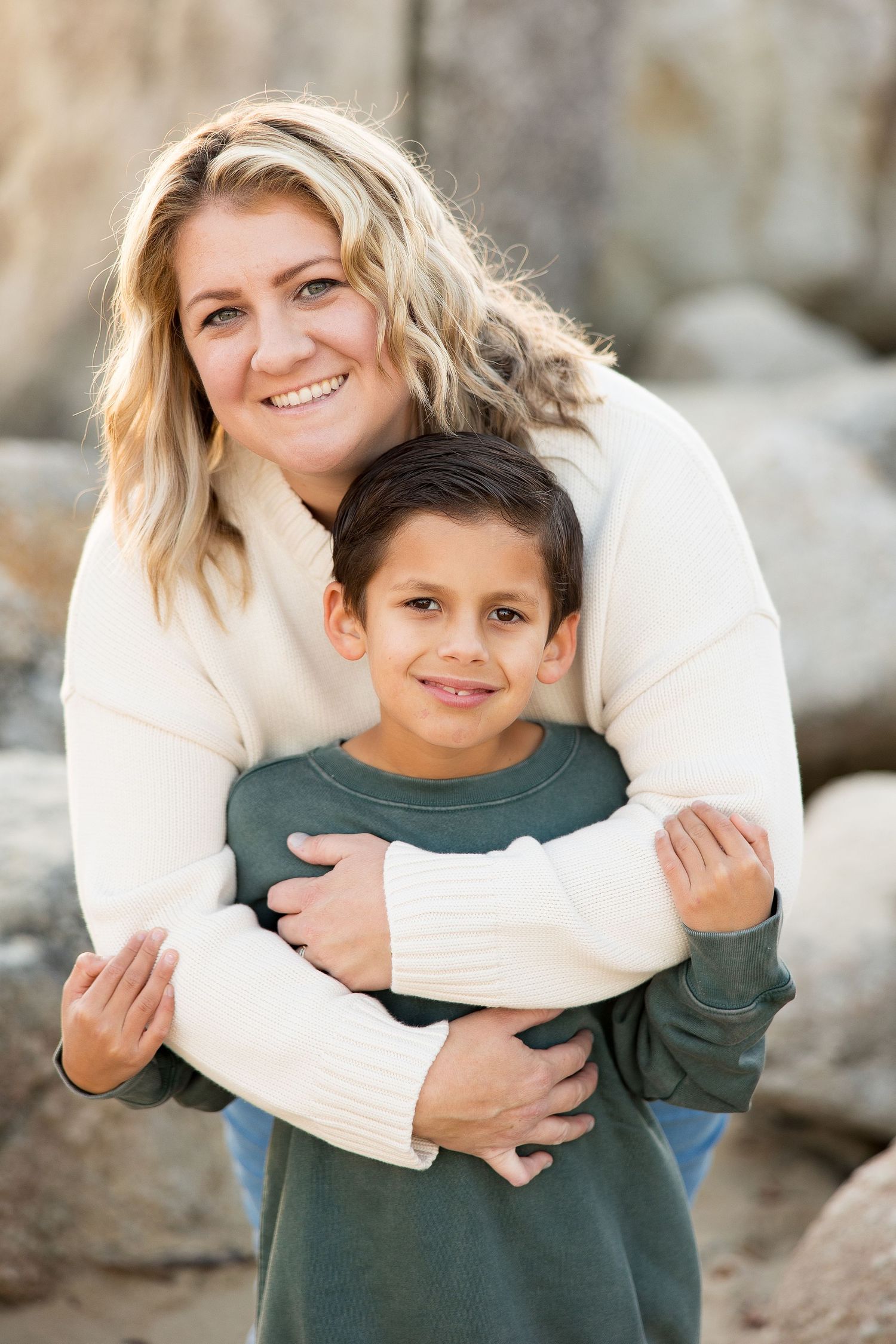 Parent and child in coordinating sweaters sharing a warm embrace against rocky backdrop.